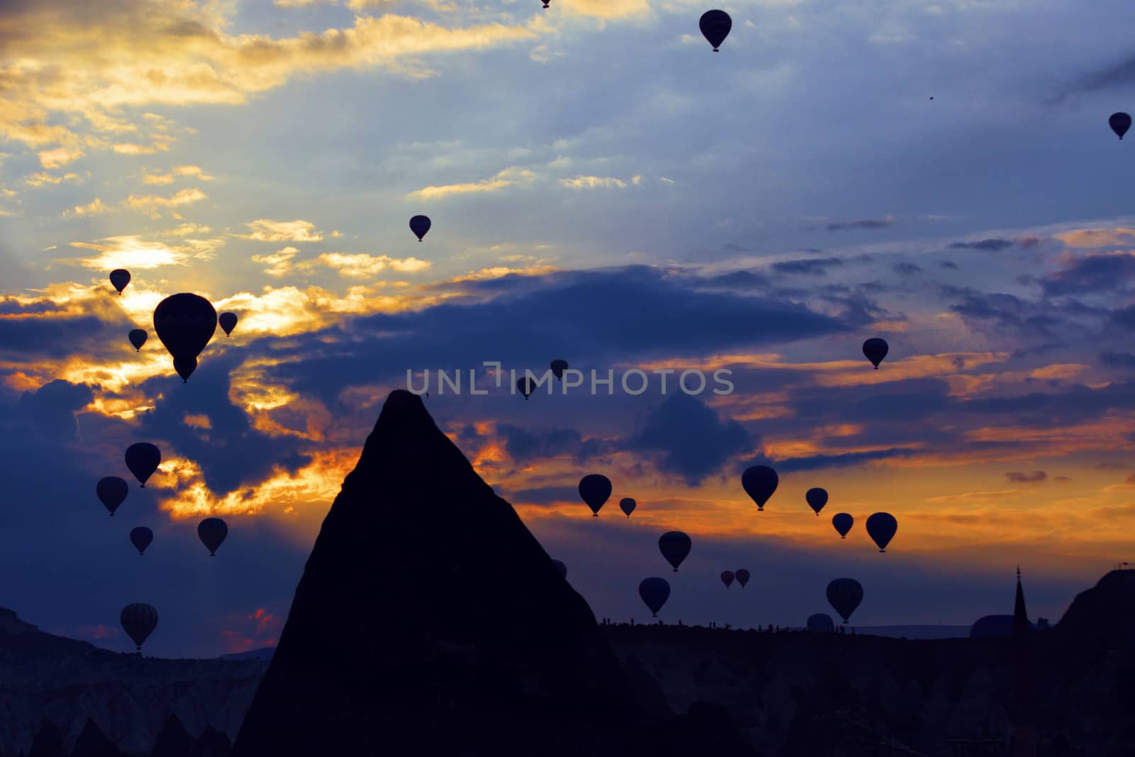 Spectacular view of dozens of flying balloons in the backlight of the early morning against the backdrop of a bright sunrise and blue sky over the conical cliffs of Cappadocia in central Turkey.