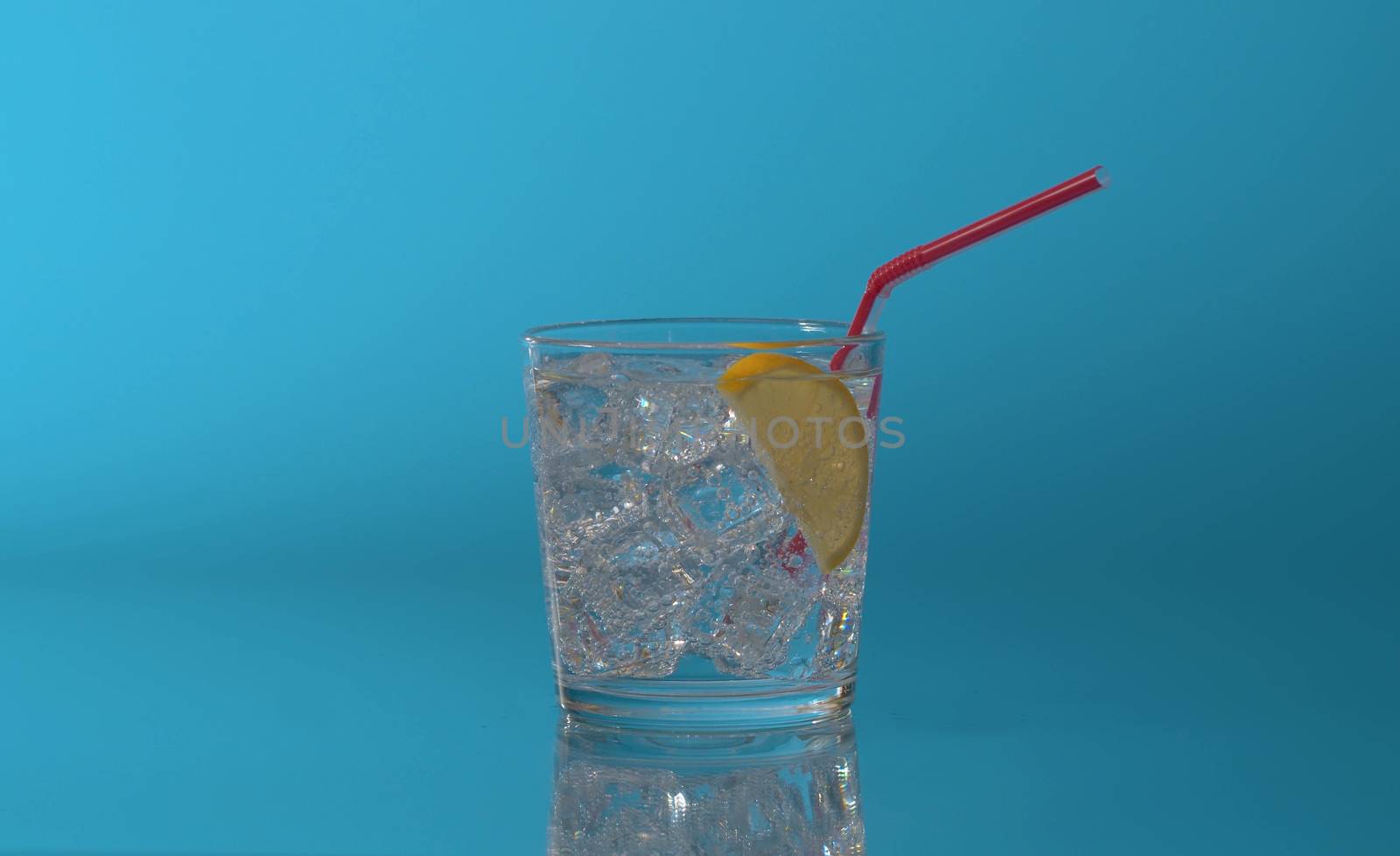 Close up tonic, soda sparkling water in a glass with ice and slice of lemon on a blue background. Refreshing mineral water