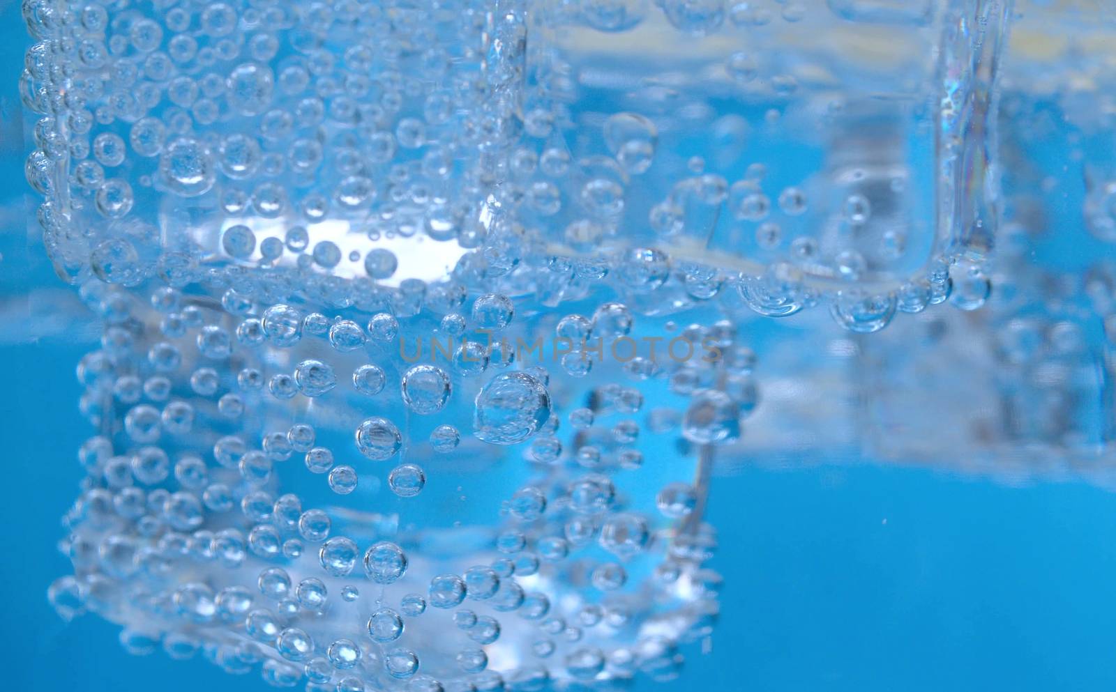 Extreme close up ice pieces in mineral water on a blue background. Tonic, soda sparkling water in a glass. Gas bubbles on the ice.