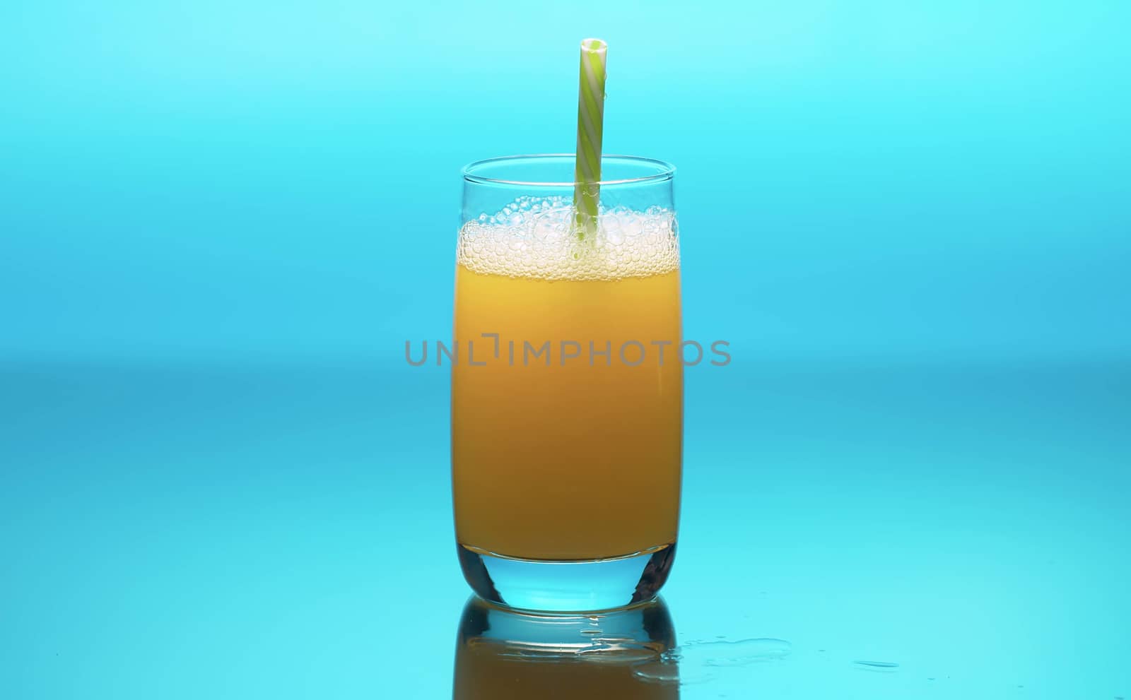 Fresh orange juice in a transparent glass on a table. Close up refreshing yellow beverage on blue background. Healthy lifestyle concept