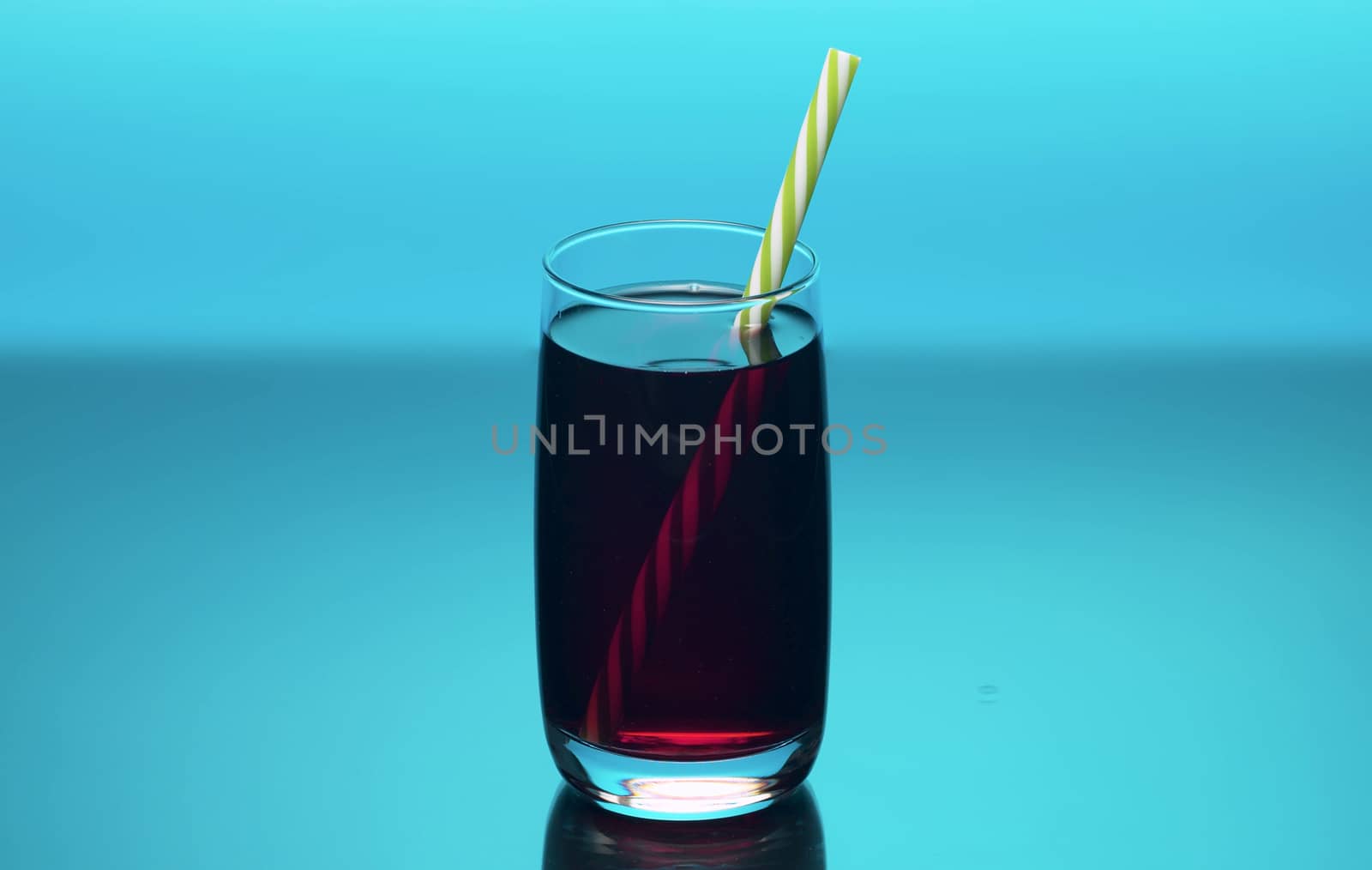 Close up cherry juice in the transperent drinking glass on blue bacground. Cherry or pomegranate or cranberry juice.