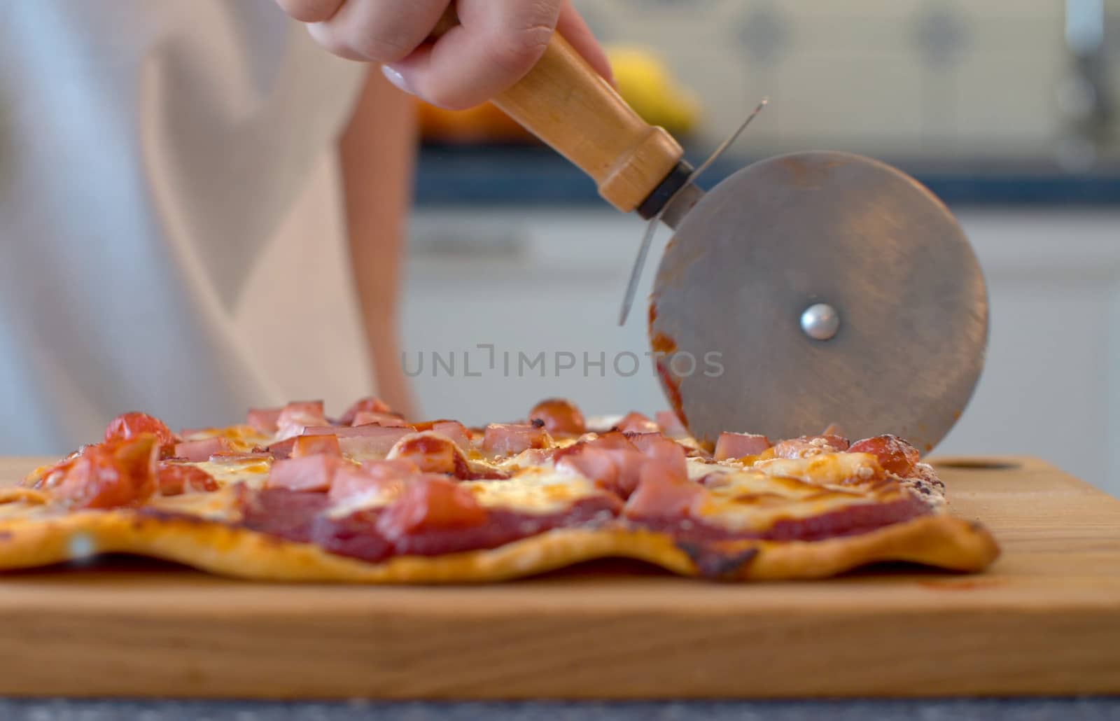Close up female hands cutting pizza with roller knife on wooden board. Preparation of traditional italian food. Food concept.