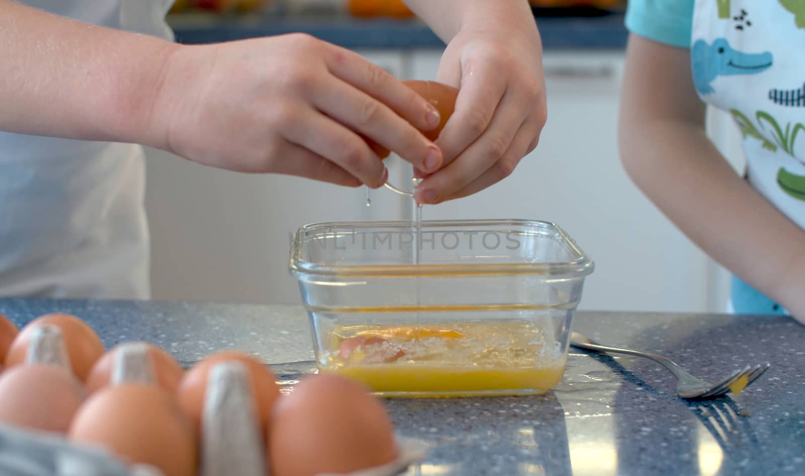 Close up childrens's hands cooking pastries in a bright kitchen. Girl breaking an egg into a glass bowl.