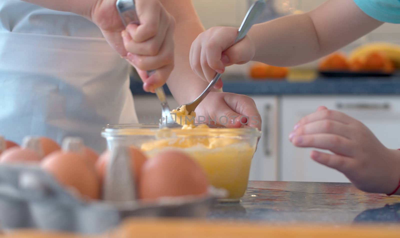 Close up hands of two children mixing butter with sugar and eggs in glass bowl. Childrens's hands cooking pastries.