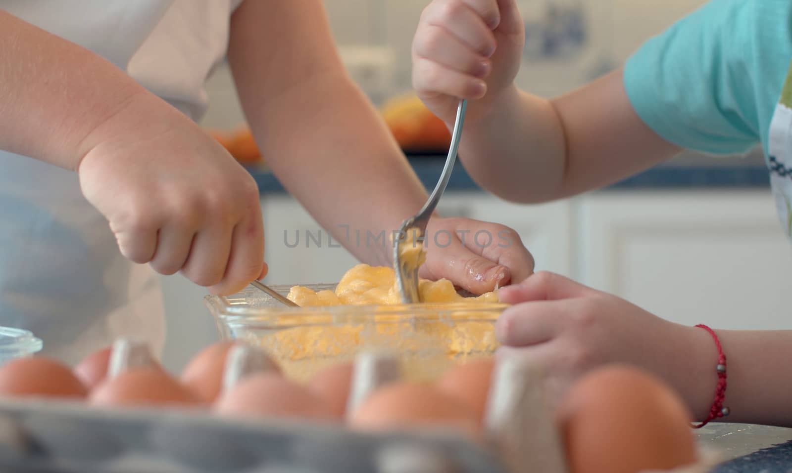 Close up hands of two children mixing butter with sugar and eggs in glass bowl. Childrens's hands cooking pastries.