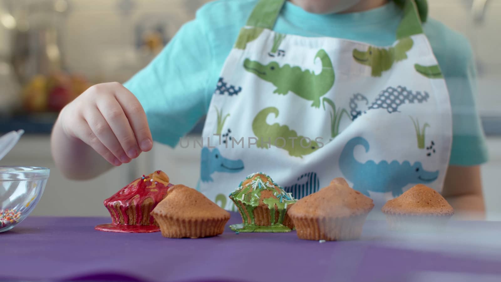 Closeup of a child's hand decorating cupcakes. Child preparing dessert in a clean bright kitchen. Cupcakes and muffins, home bakery concept