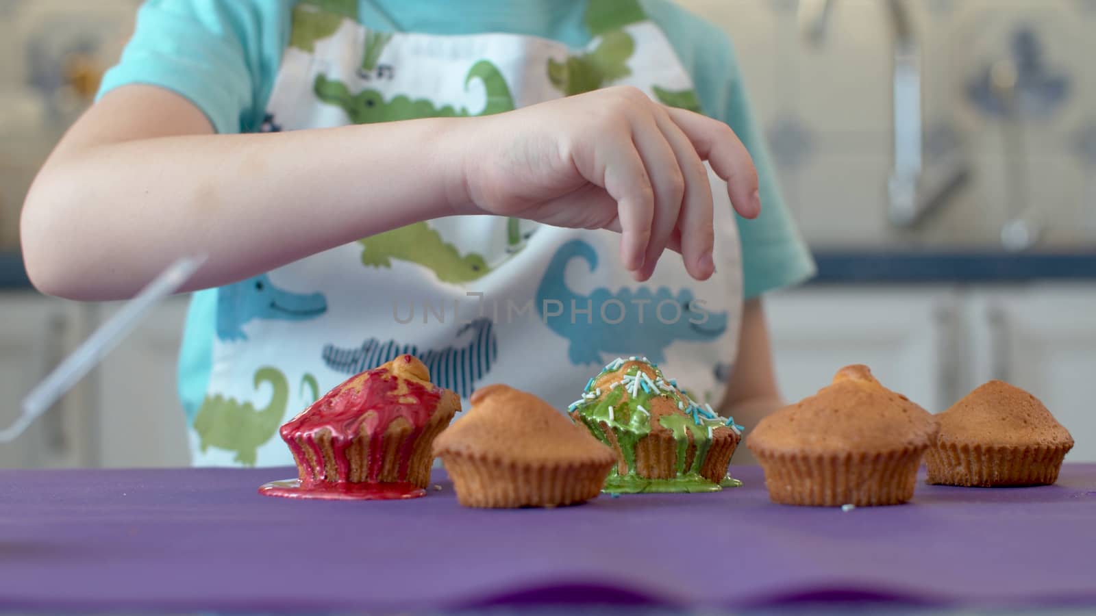 Closeup of a child's hand decorating cupcakes. Child preparing dessert in a clean bright kitchen. Cupcakes and muffins, home bakery concept