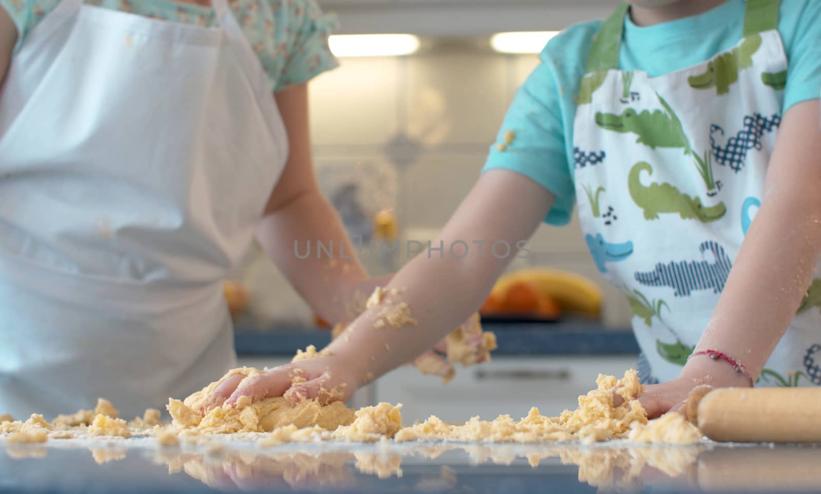 Close up child's hands in the dough. Boy gathering the dough from the table together. Kids cooking in bright kitchen.