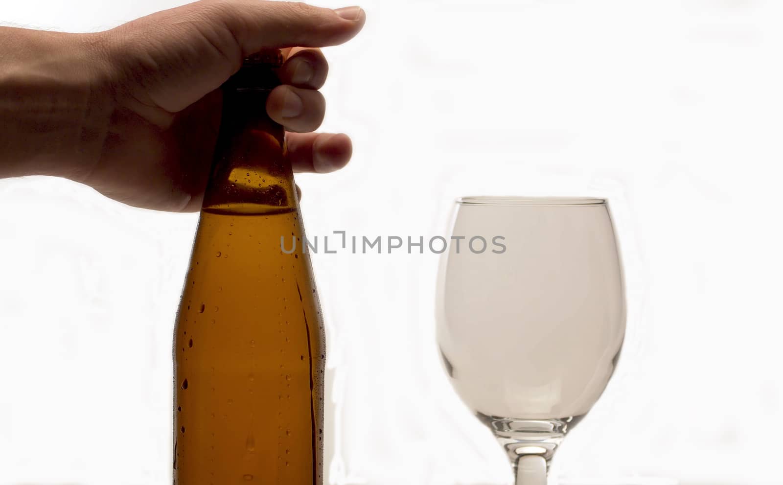 Close up male hand putting misted bottle of cold beer on the table. White background. Drops of water flowing down. Craft beer closeup