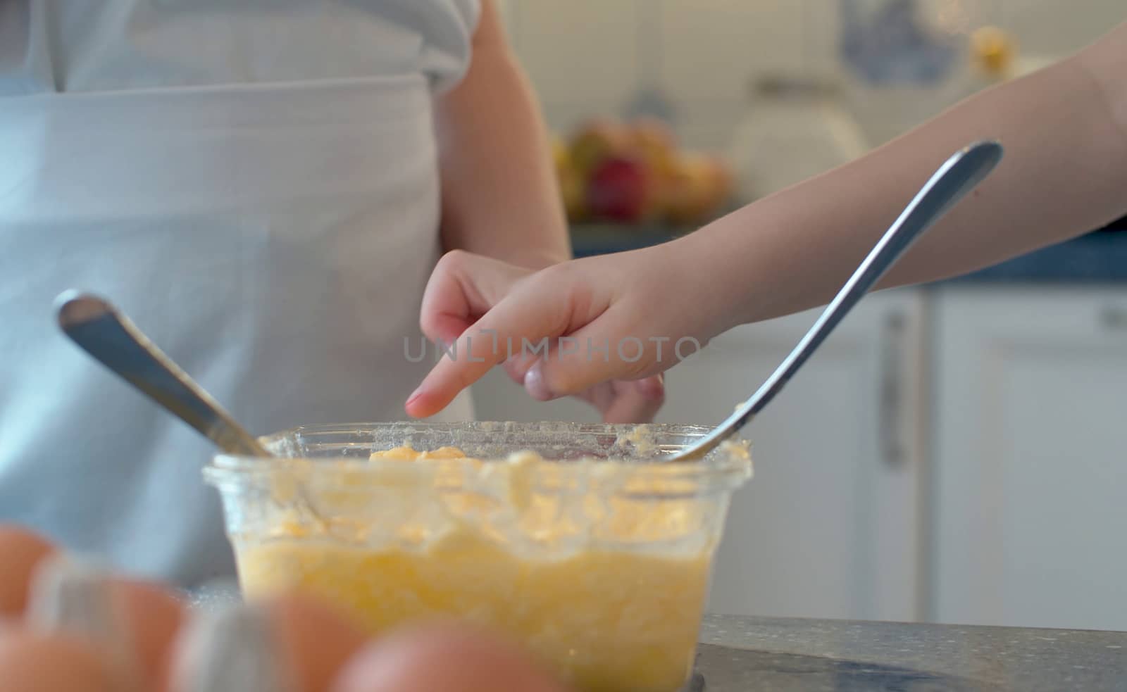 Close up hand of child tasting dough. Children cooking pastries in bright kitchen