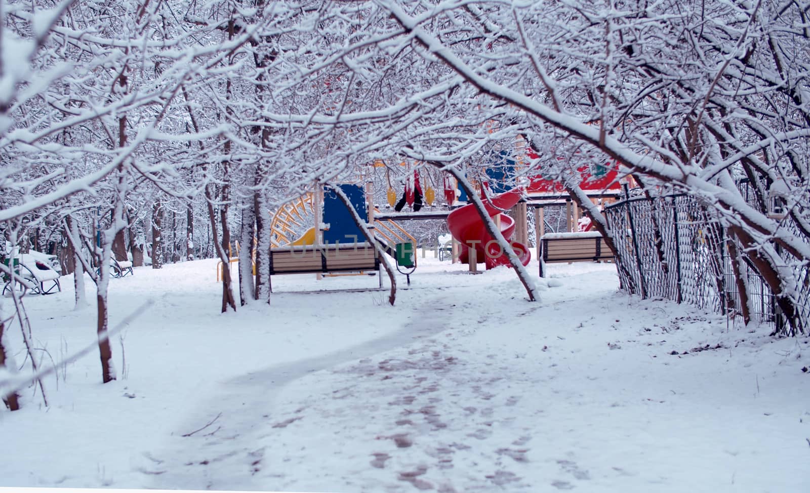 Kid playing on the playground in winter. Trees under the snow, snowfall in the park.