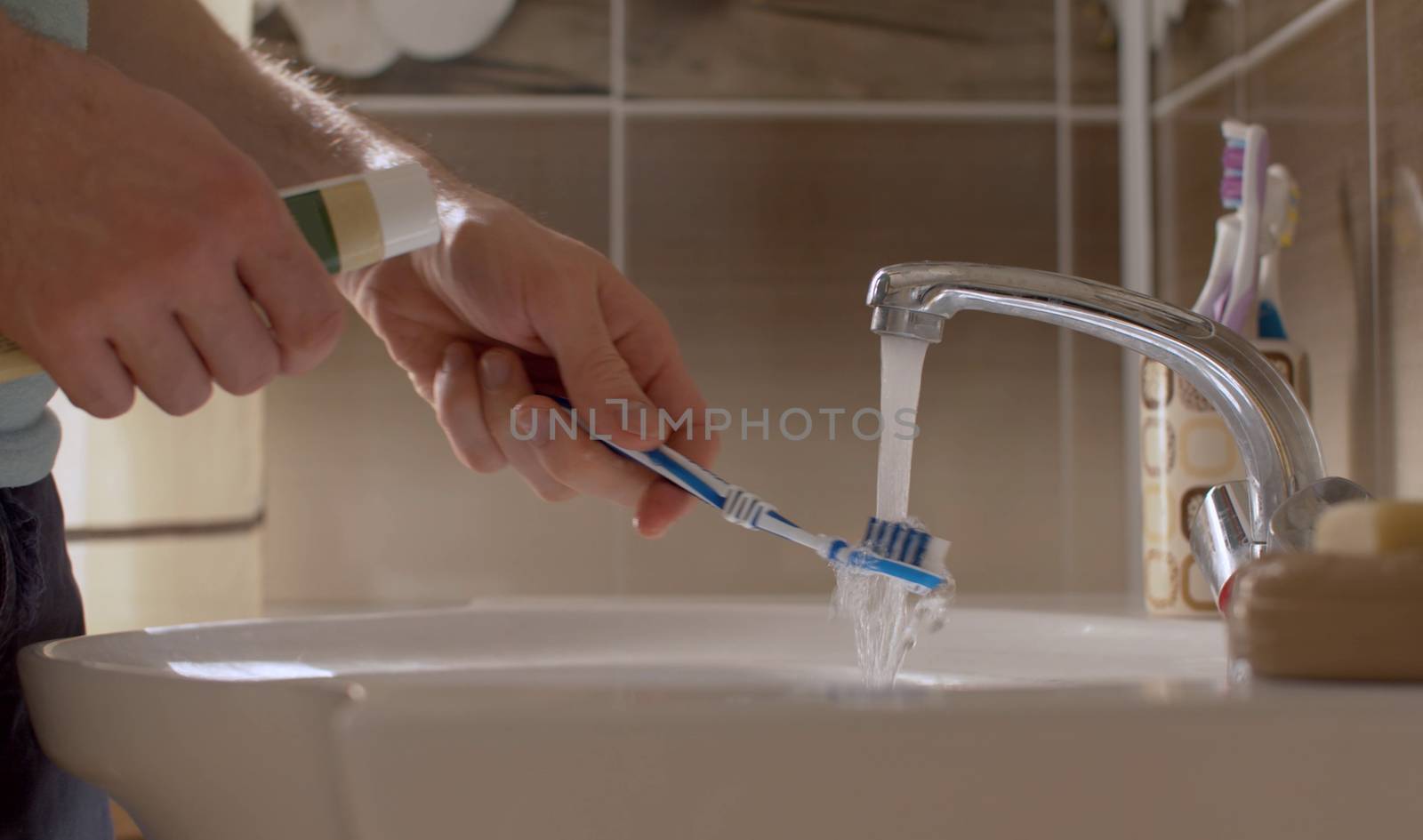 A young man brushes his teeth in a beautiful bathroom. Close up male hands with tooth paste and tooth brush. Daily Hygiene Procedures