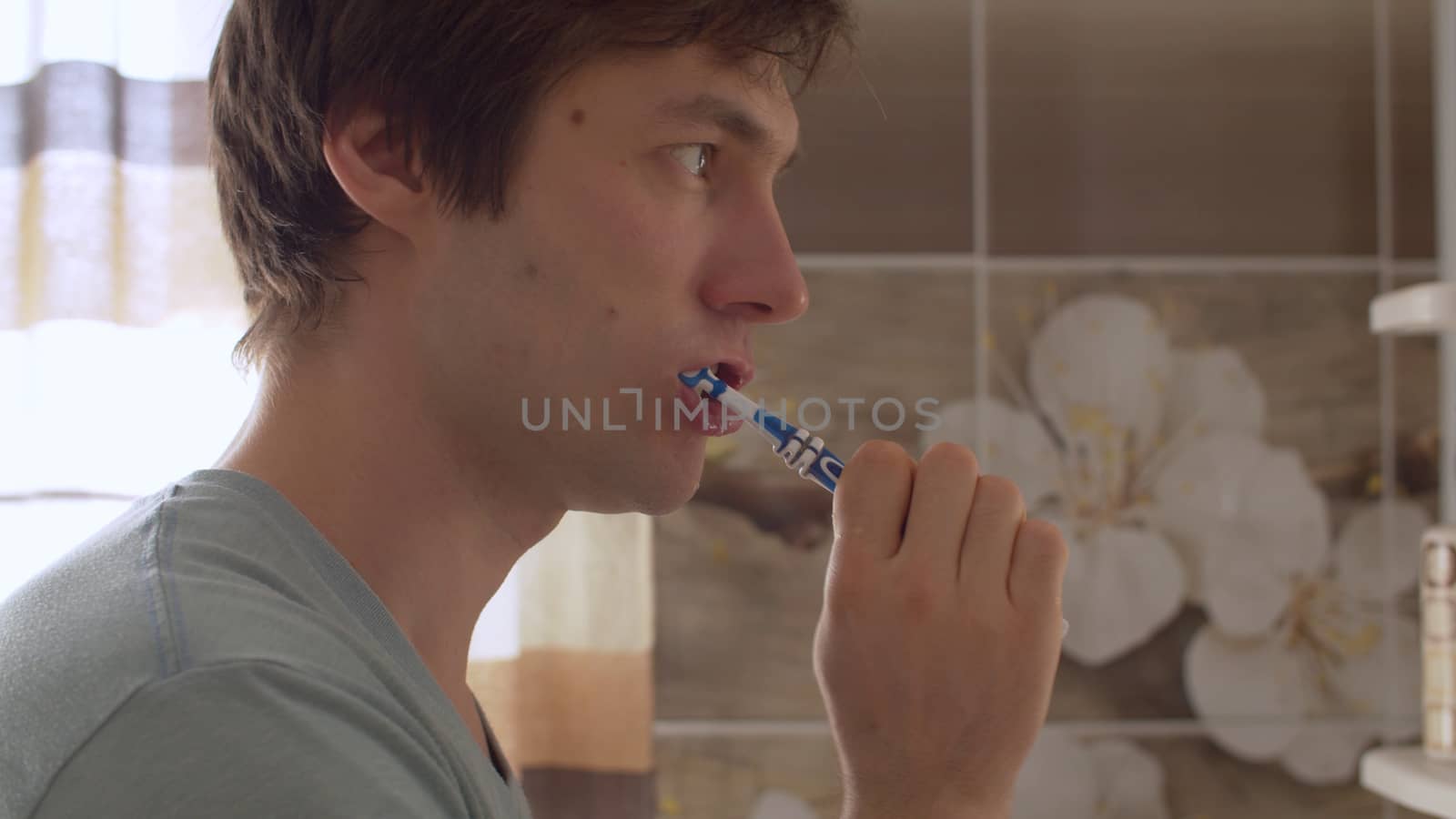 A young man brushes his teeth in a beautiful bathroom. Close up male portrait. Daily Hygiene Procedures