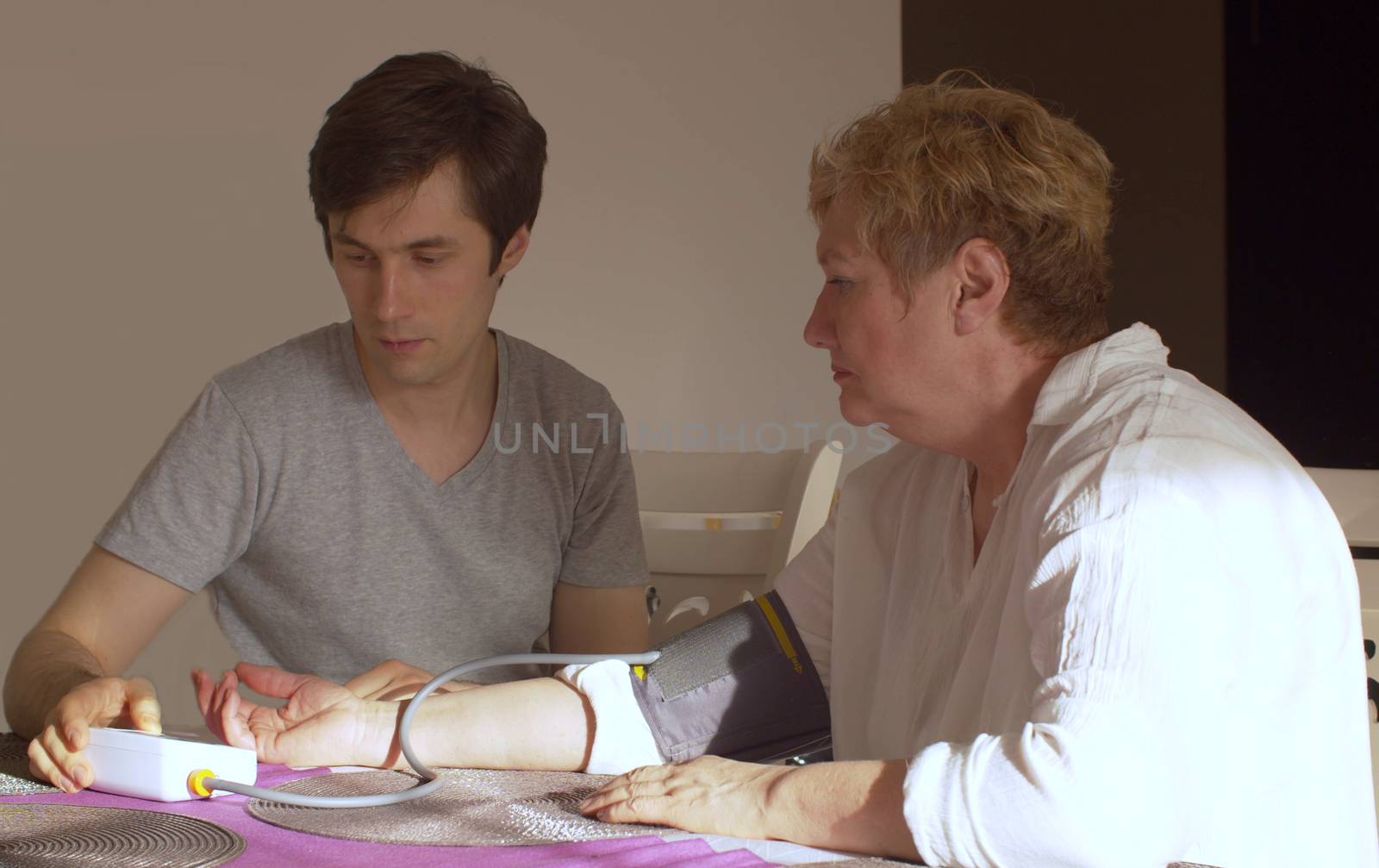 Son measuring blood pressure of an elderly mother at home. Young man helping senior woman to check pressure using medical tonometer. Healthcare concept