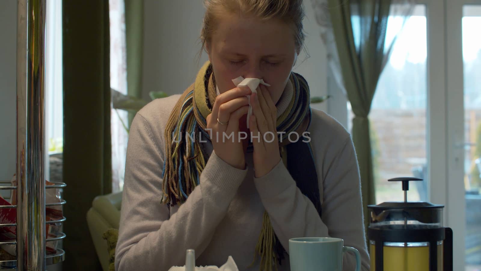 Young woman with a cold and a stuffy nose blows her nose in a napkin. Health care and therapy concept