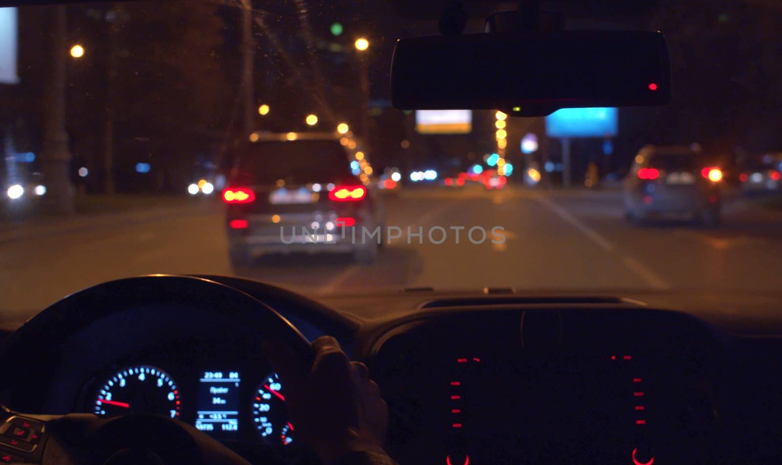 Close up man's hands on the steering wheel. Dashboard lights up inside the dark interior of a car. POV night driving.
