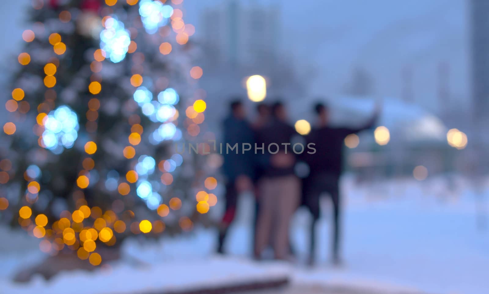 Blurry unrecognizable people take selfie near the Christmas tree outdoors. City holiday decorations.