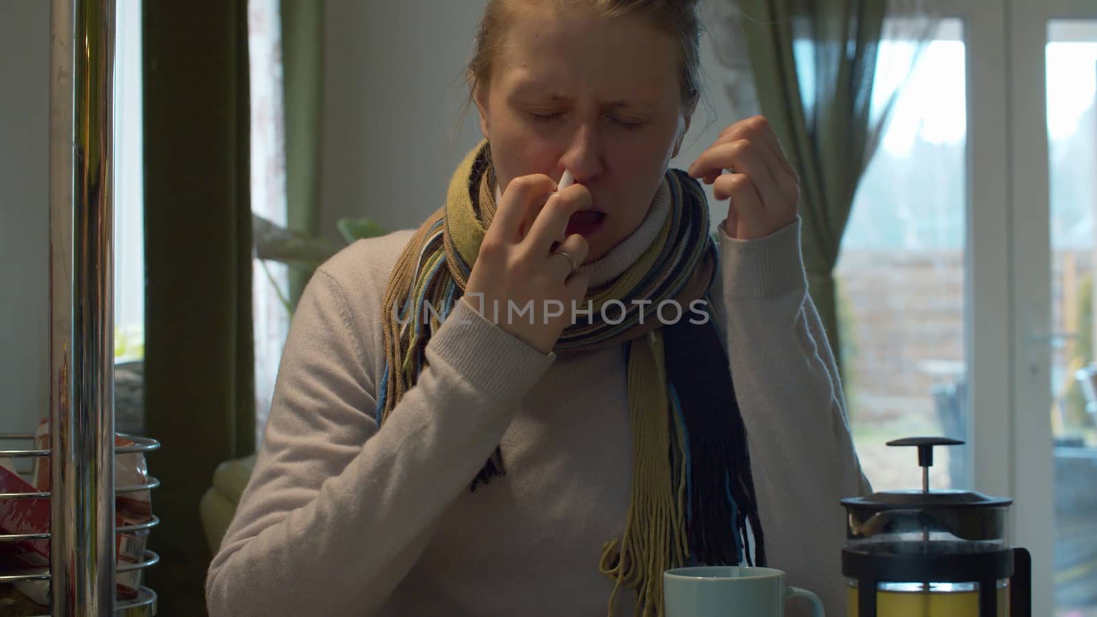Young woman feeling blocked nose while cold and flu spraying nasal spray for treatment respiratory disease. The medicine is unpleasant to her - she frowns and sighs. Health care and therapy concept