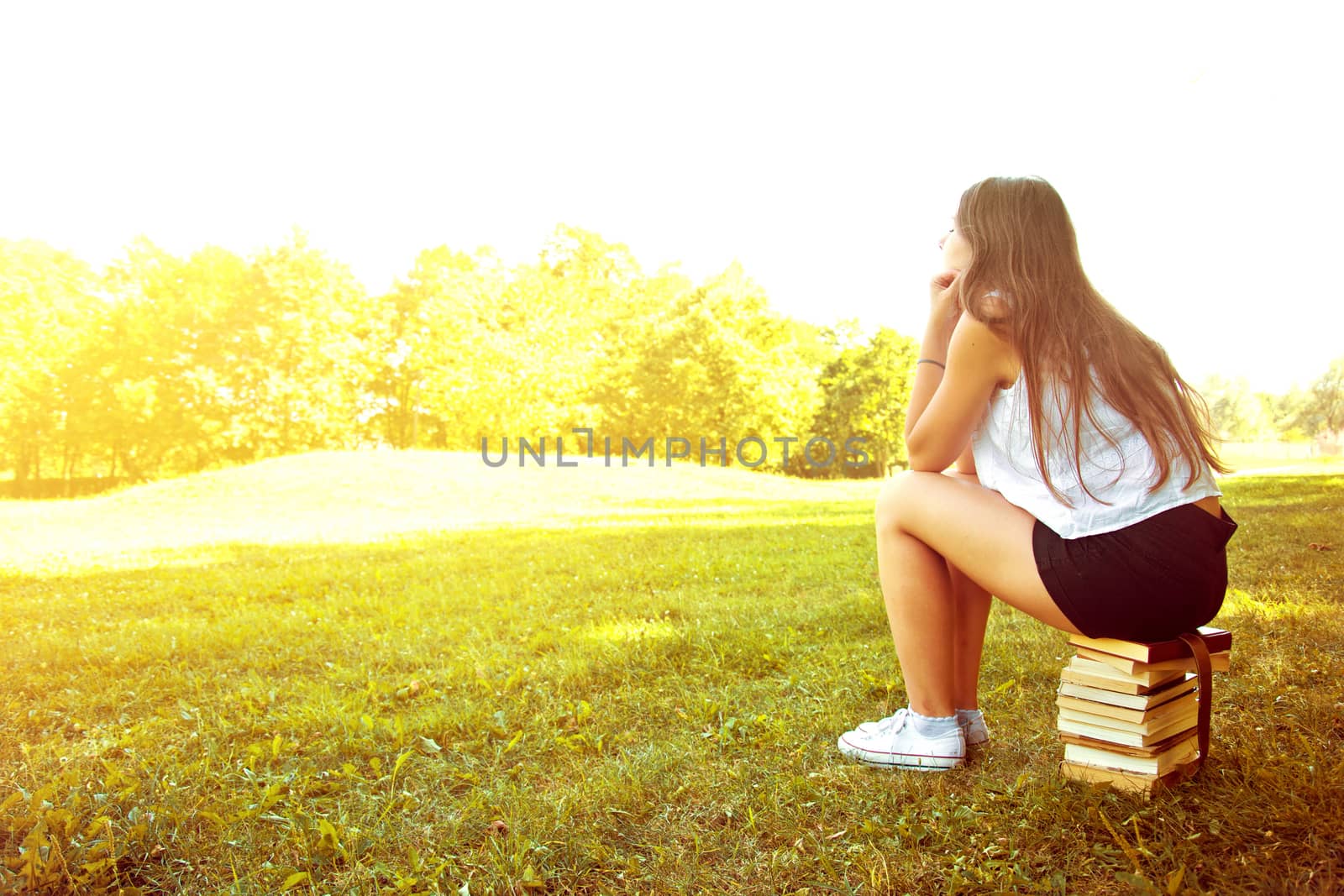 Attractive female college student daydreaming and sitting on the stack of books. Education. Back to school conceptual image.