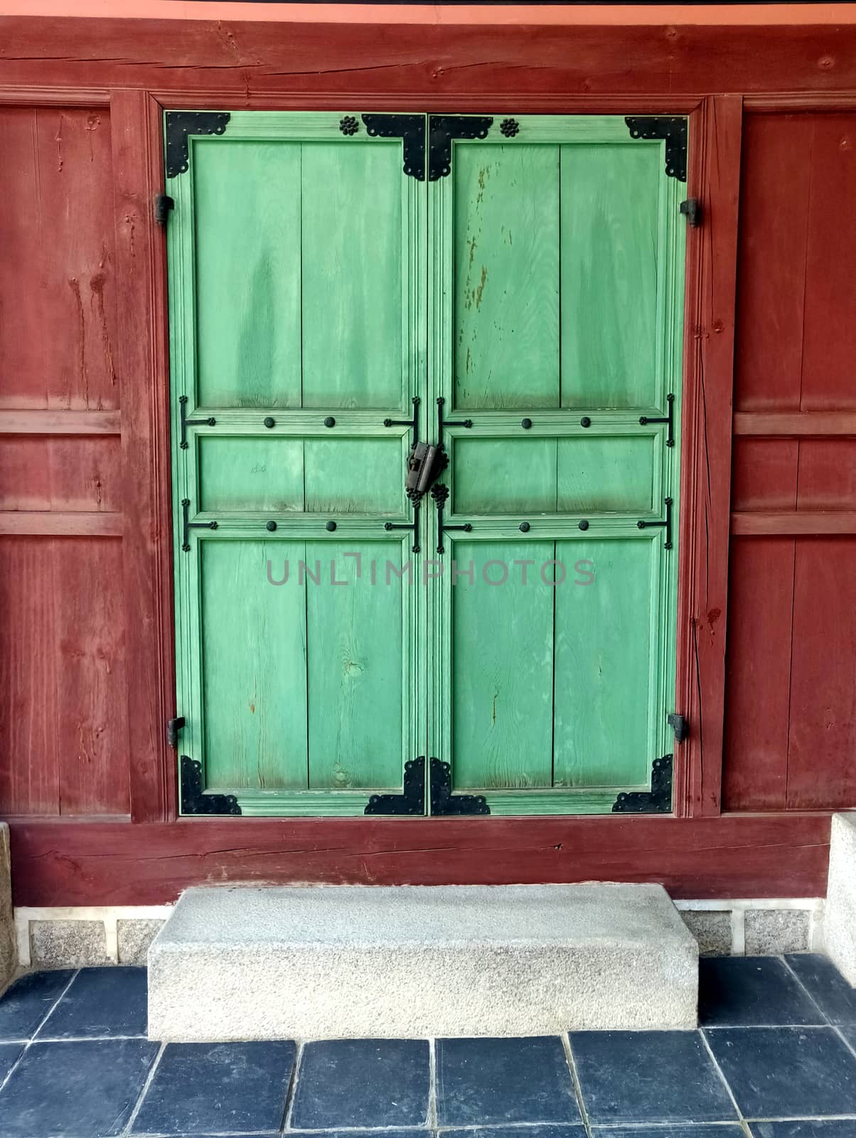 A wooden green door with red wall with an old ancient lock and blue floor in the front