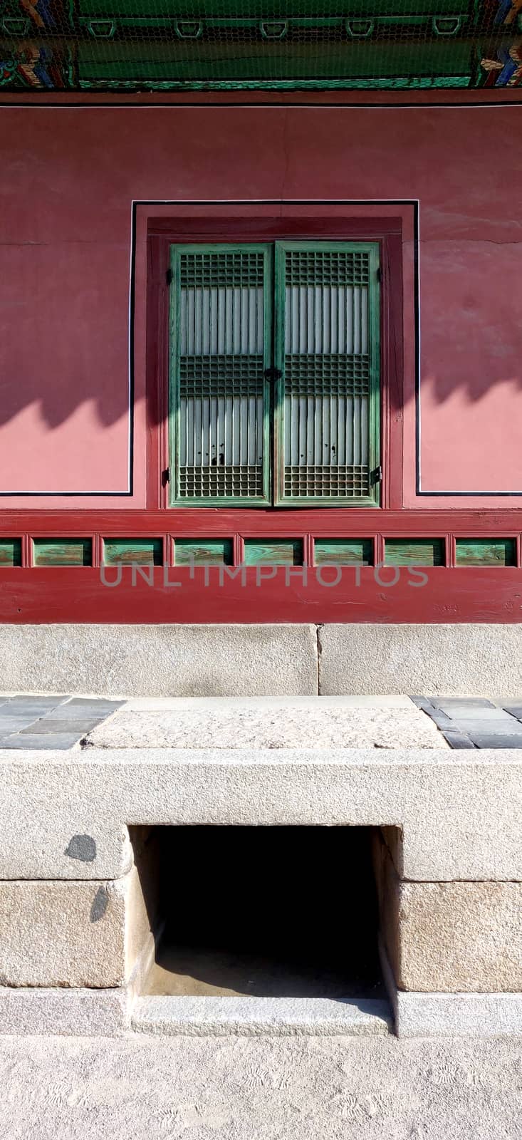A wooden ancient green door and red wall with a cement bench made in front of it in traditional houses in Korea