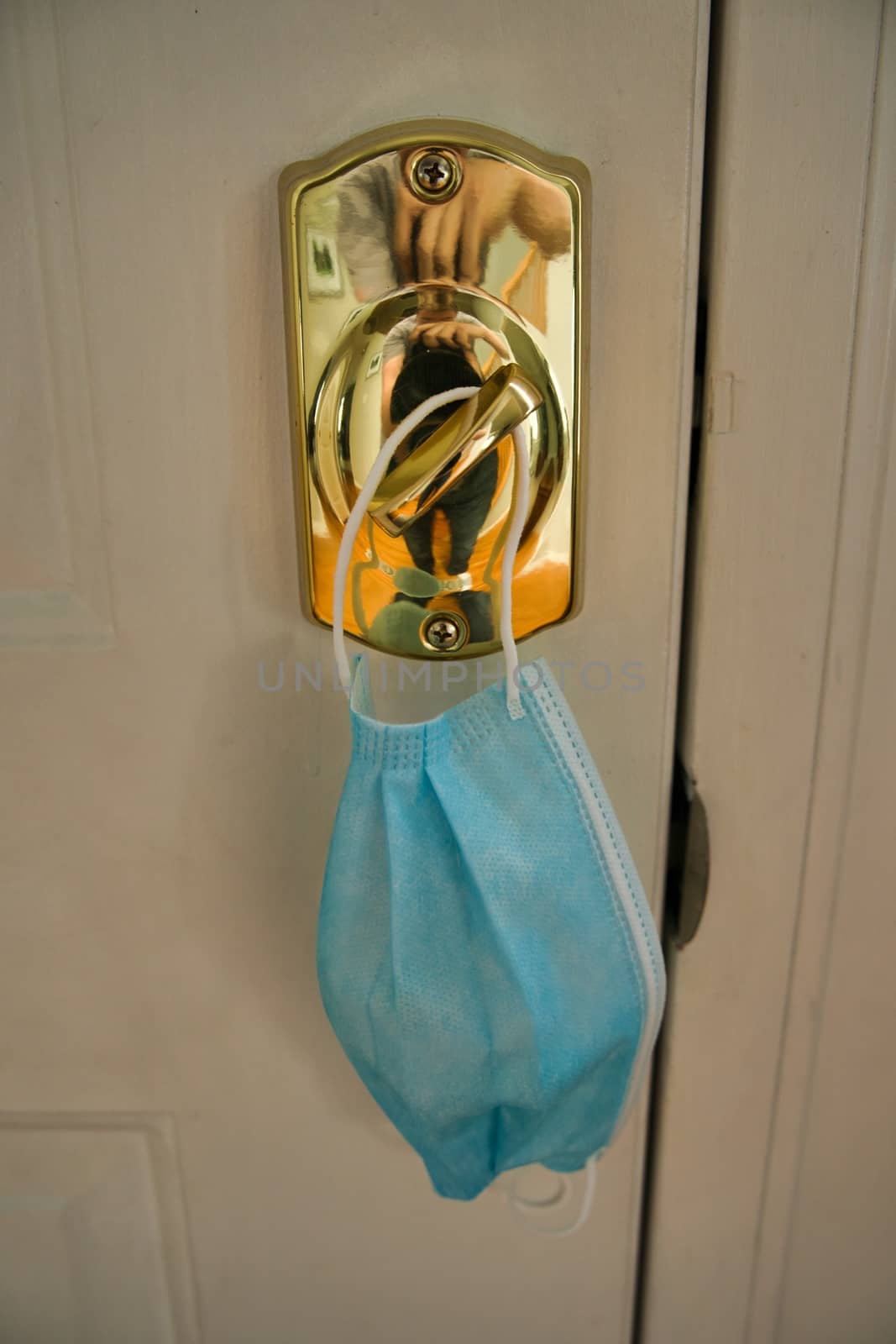 Blue mask hanging from lock as a reminder to wear facemask when leaving home to protect face, nose, and mouth from coronavirus