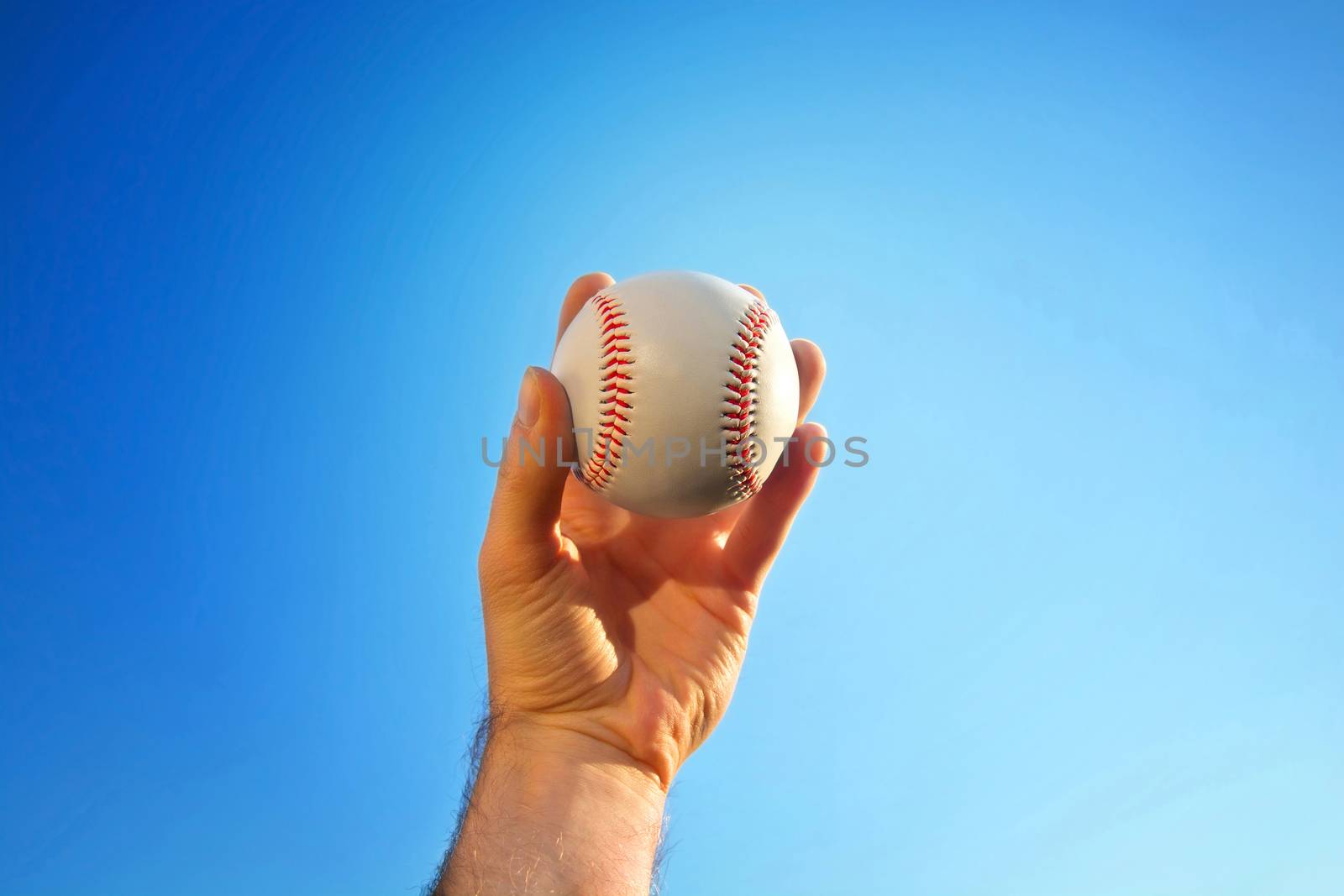 Baseball game. Baseball ball holding by hand against blue clean sky.