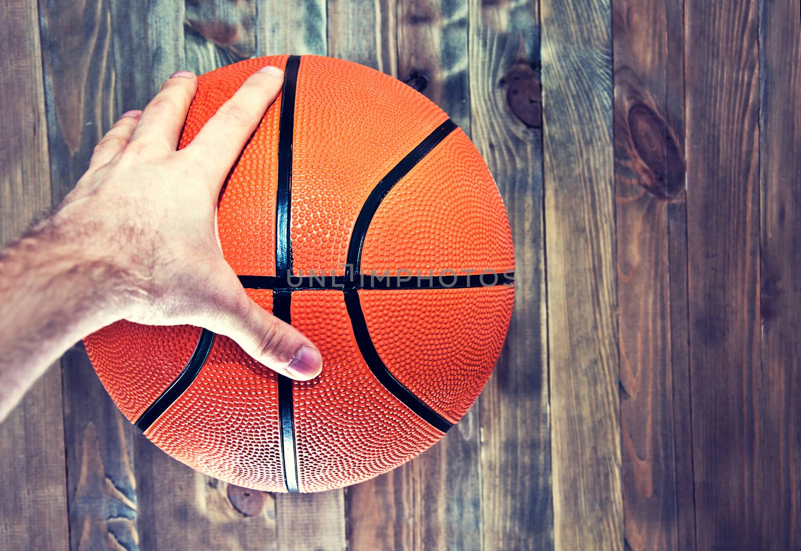 Basketball ball on wooden hardwood floor in the basketball court grabbing by hand. Retro vintage picture. Sport concept.
