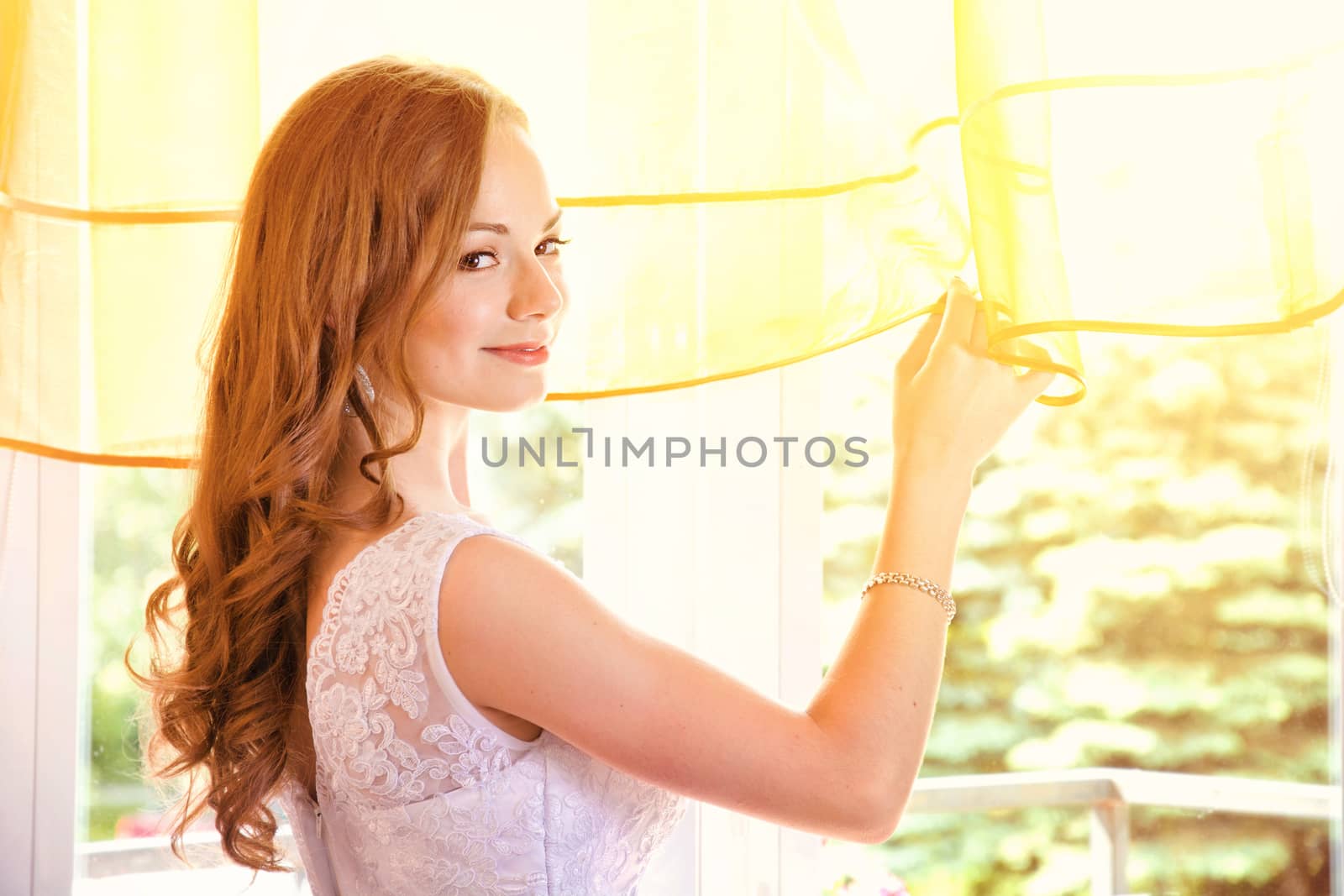 Young beautiful bride in wedding dress looking through the window. Marriage and wedding concept image.