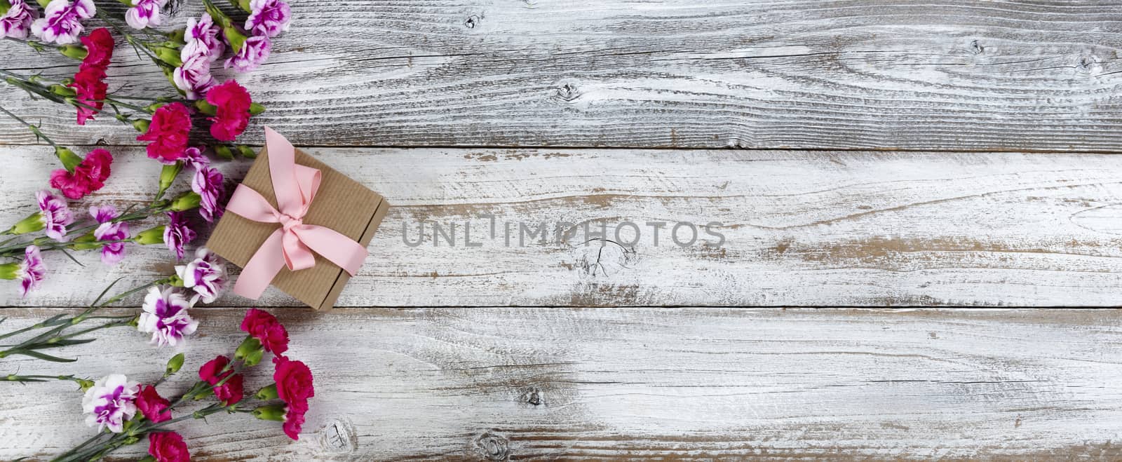 Left side border of carnation flowers and Mothers day gift box on white rustic wooden background with copy space. Top view in flat lay format.   
