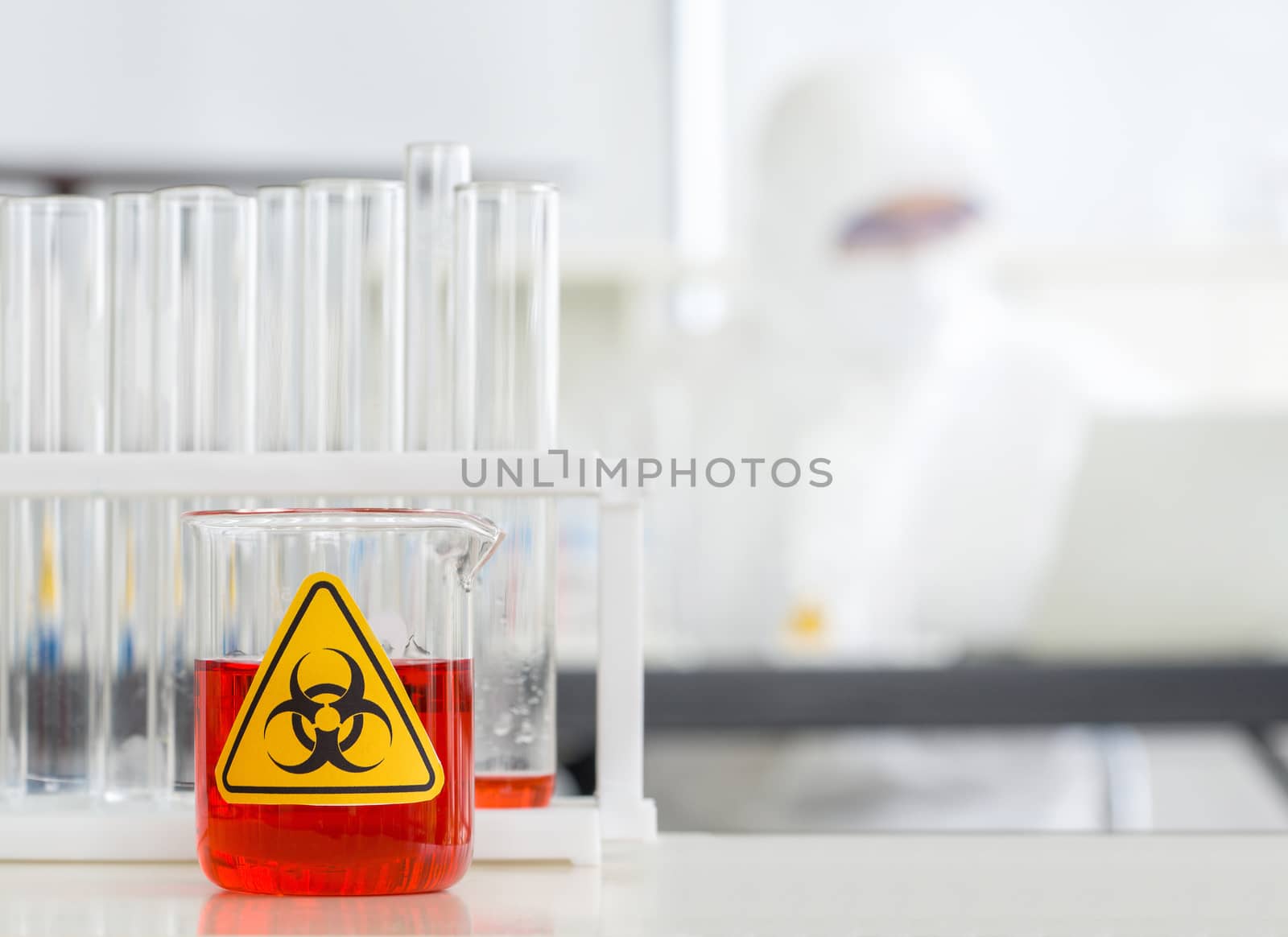 Beaker contains red liquid chemicals on a white laboratory table by chadchai_k