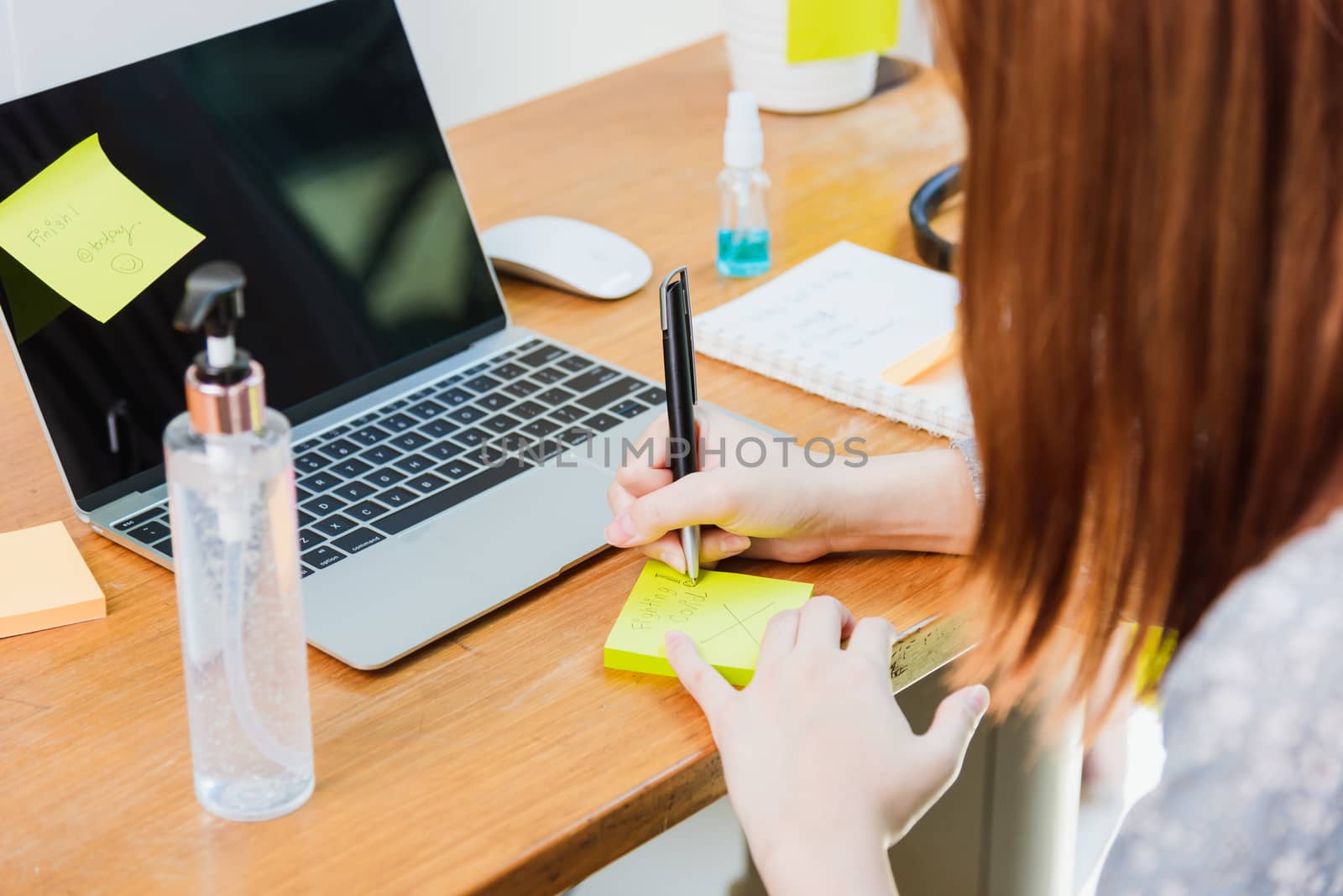 Asian young business woman wearing face mask protective working from home office with laptop computer he quarantines disease coronavirus or COVID-19 and write note stick memory work today