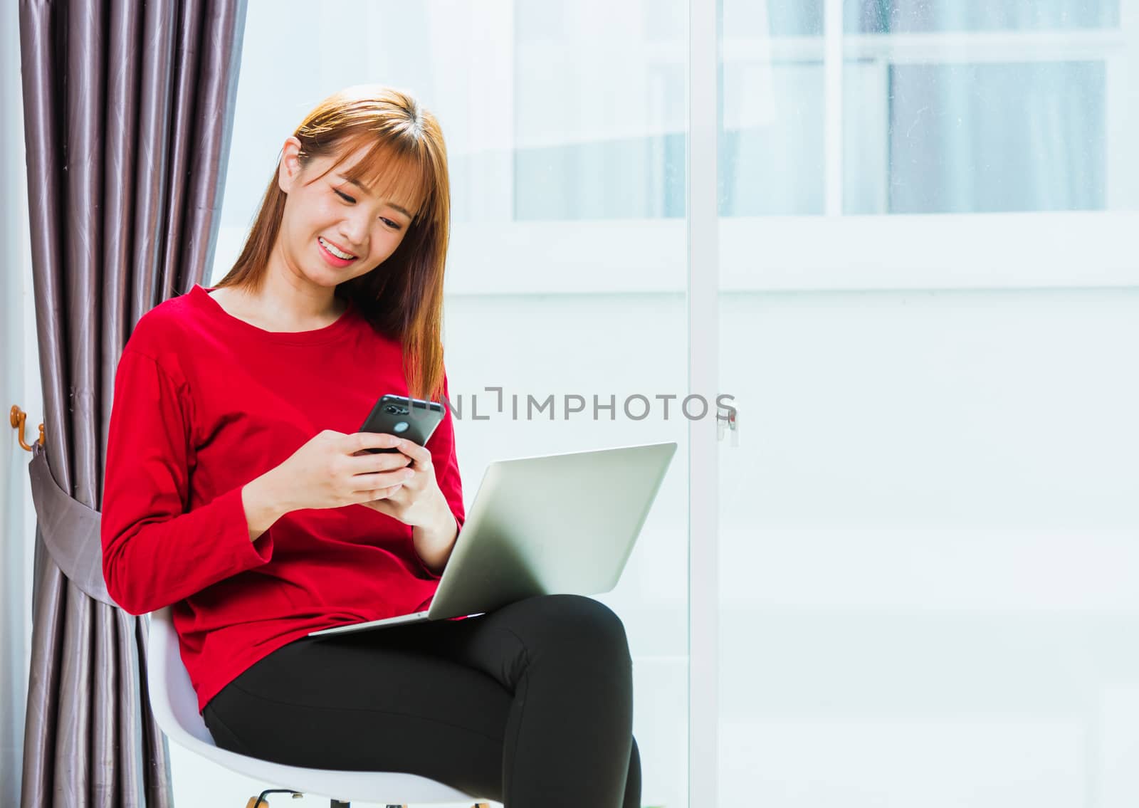 Woman smiling using mobile phone while typing message text durin by Sorapop