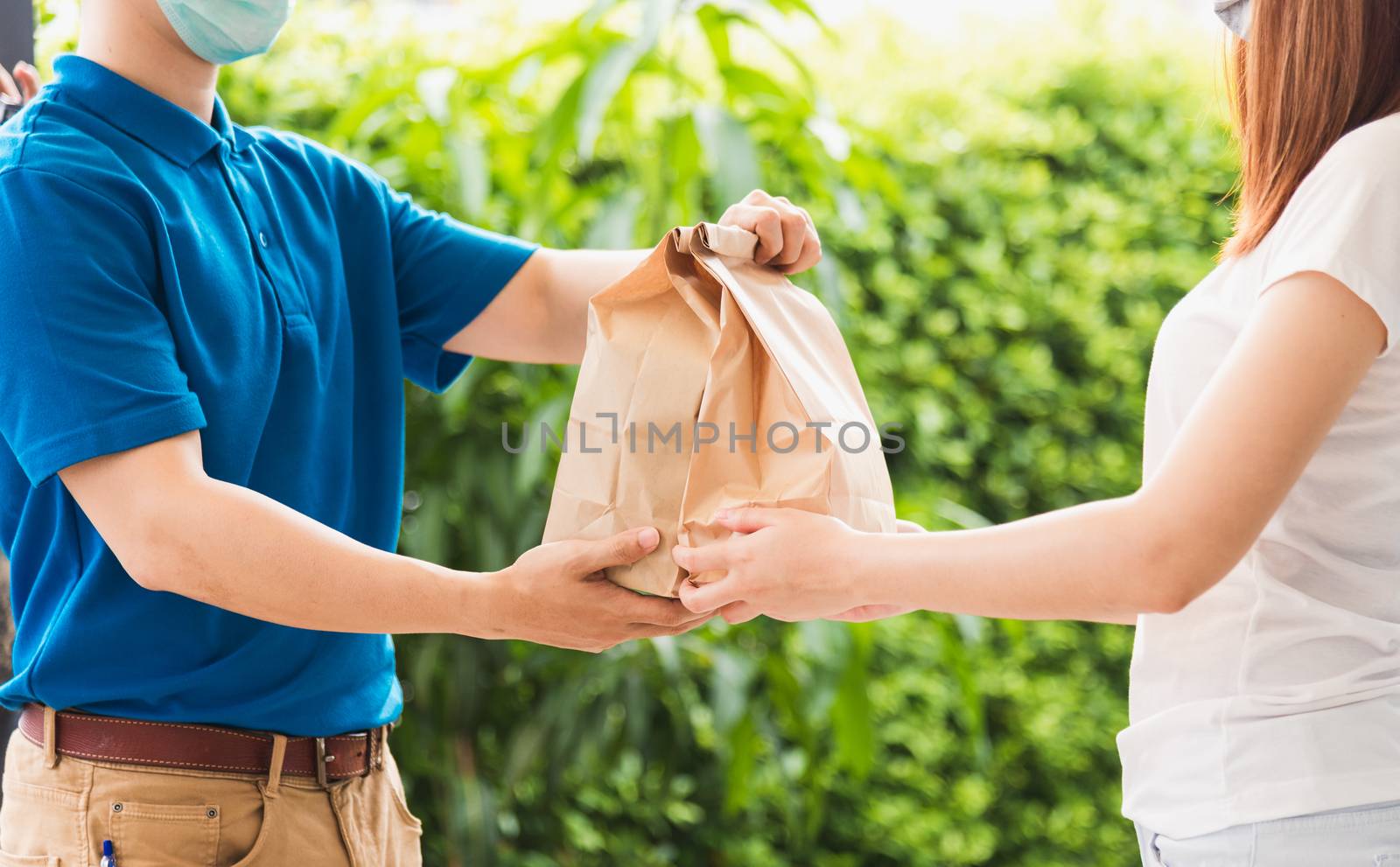 Asian delivery express courier young man giving paper bags fast food to woman customer receiving both protective face mask, under curfew quarantine pandemic coronavirus COVID-19