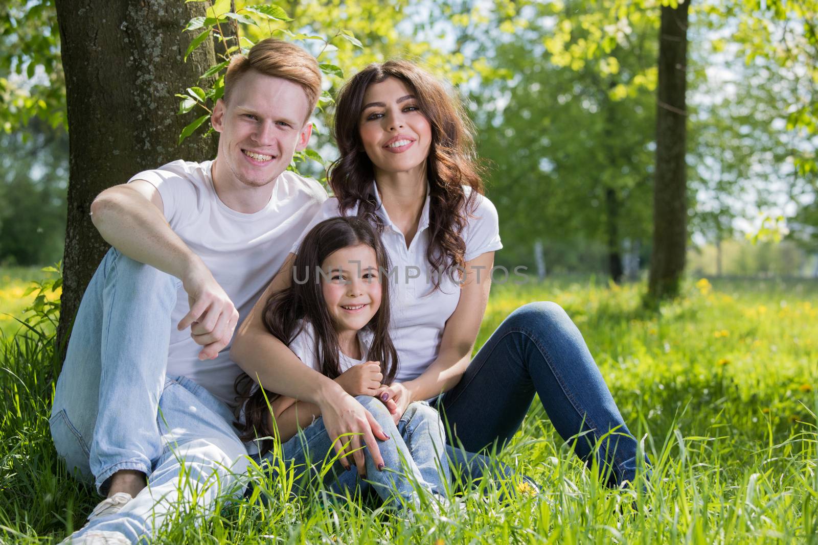 Family of three sitting on spring park meadow grass being happy