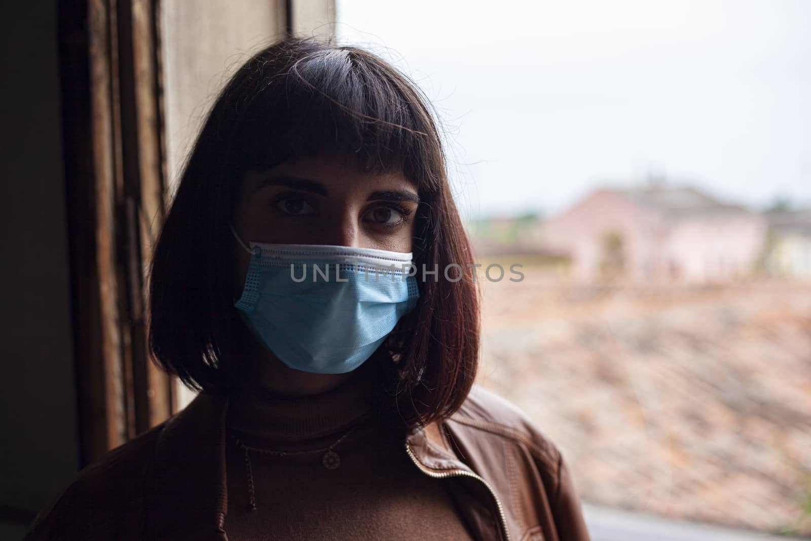 Girl with medical mask at window in her home during covid quarantine period