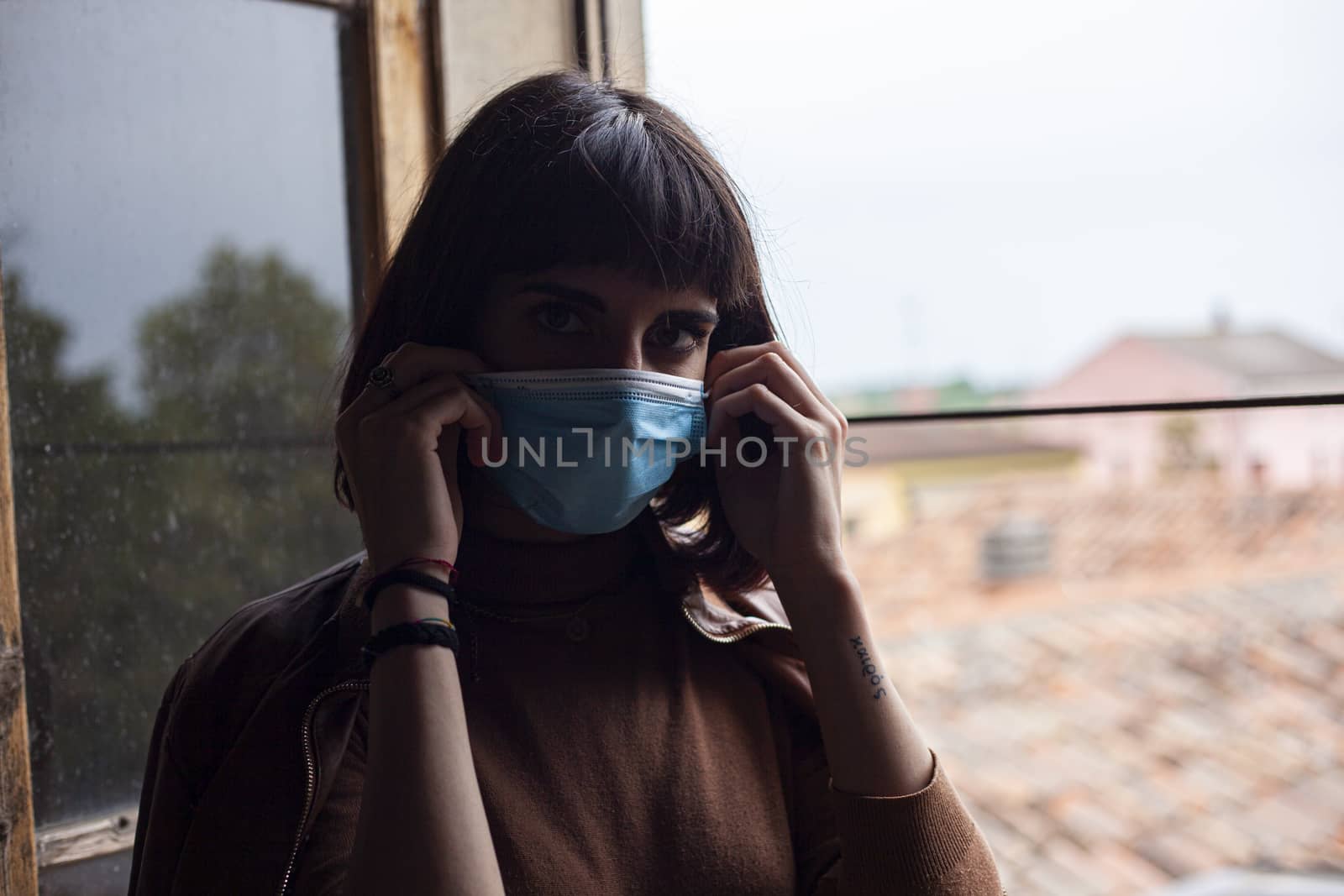 Girl with medical mask at window in her home during covid quarantine period