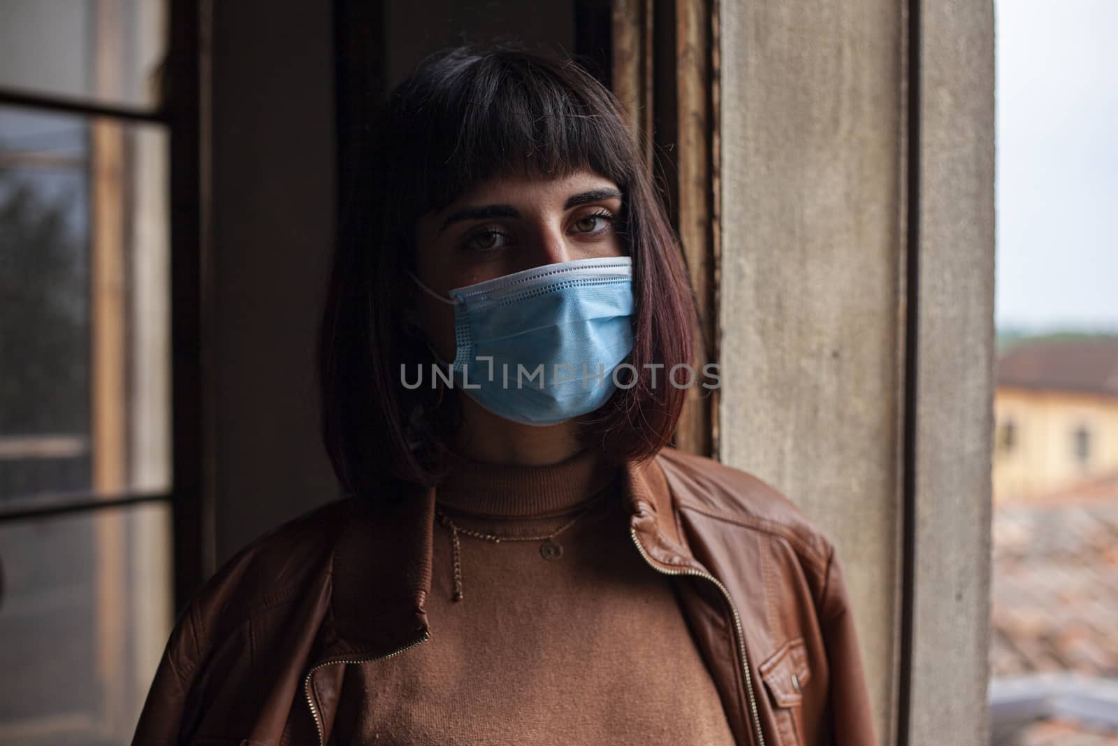 Girl with medical mask at window in her home during covid quarantine period