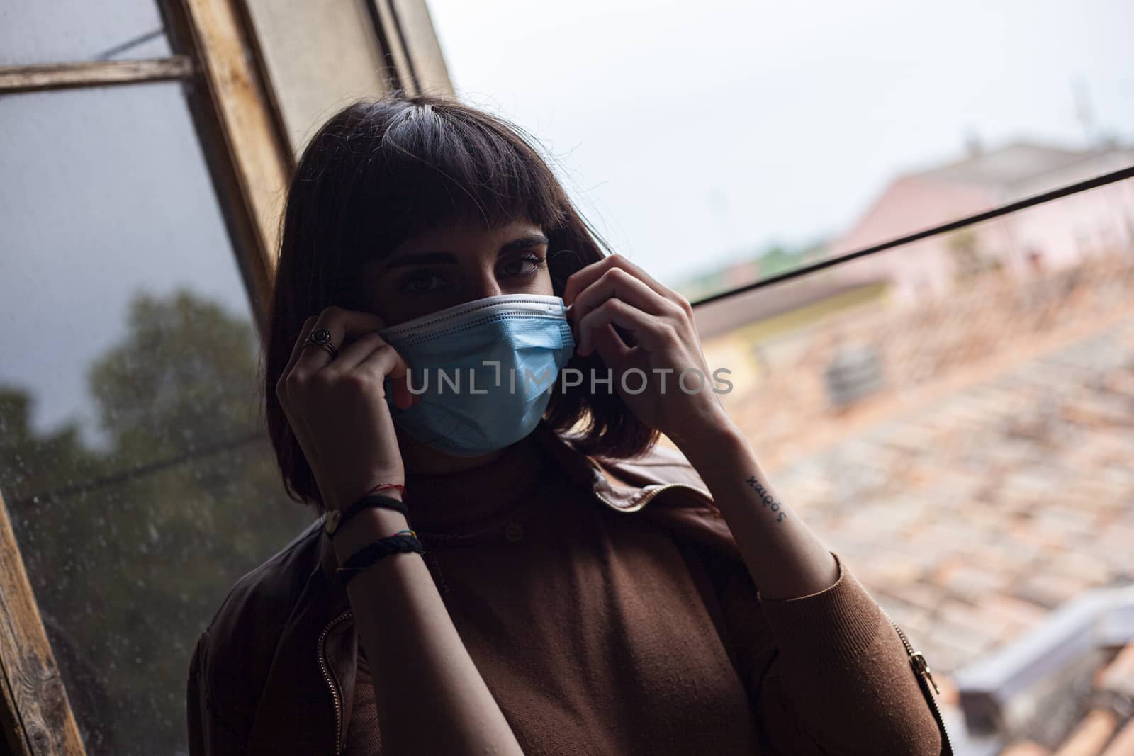 Girl with medical mask at window in her home during covid quarantine period