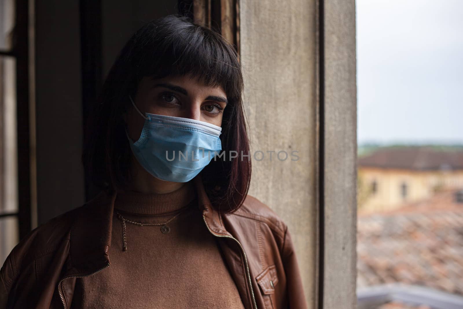 Girl with medical mask at window in her home during covid quarantine period