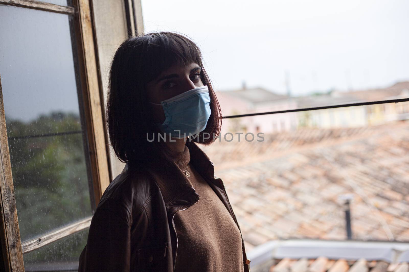 Girl with medical mask at window in her home during covid quarantine period