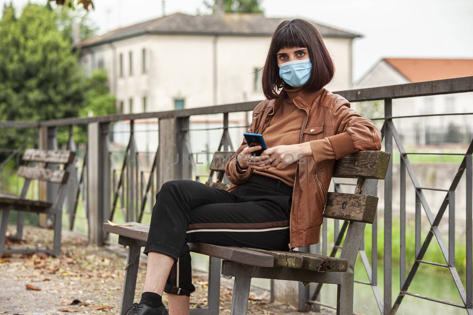 Portrait of a Girl with medical mask at park with smartphone during covid quarantine in Italy