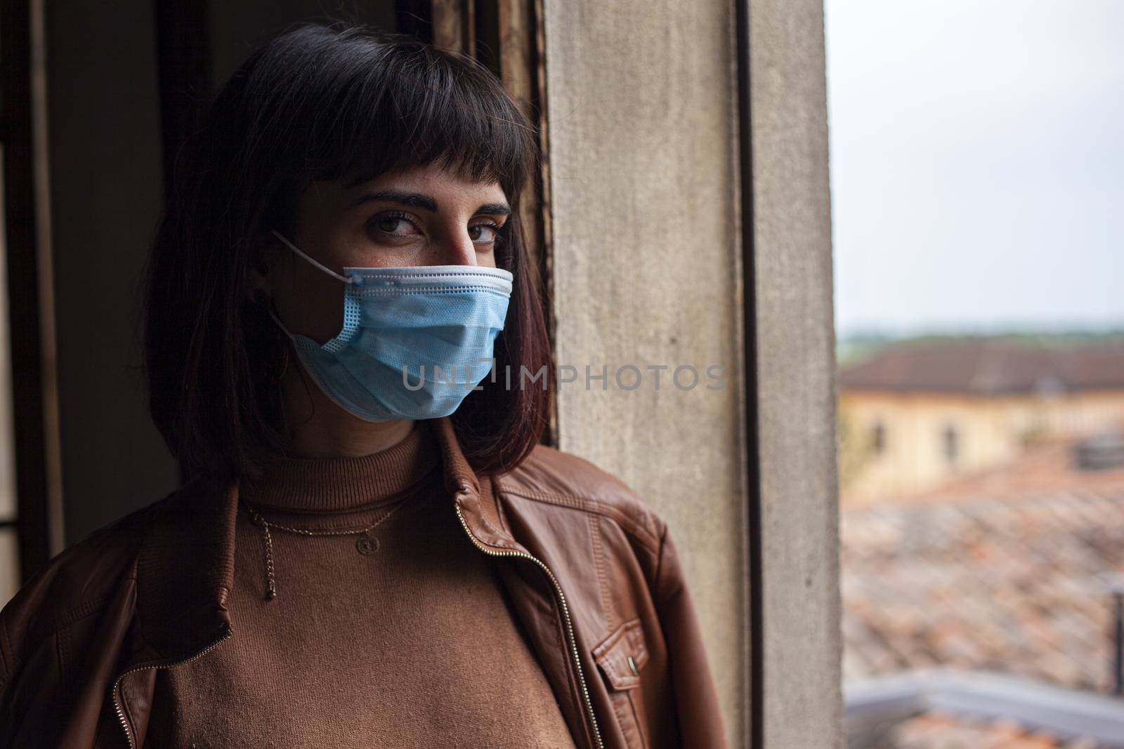 Girl with medical mask at window in her home during covid quarantine period