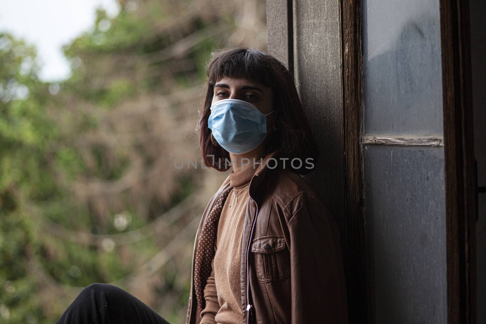 Girl with medical mask at window in her home during covid quarantine period