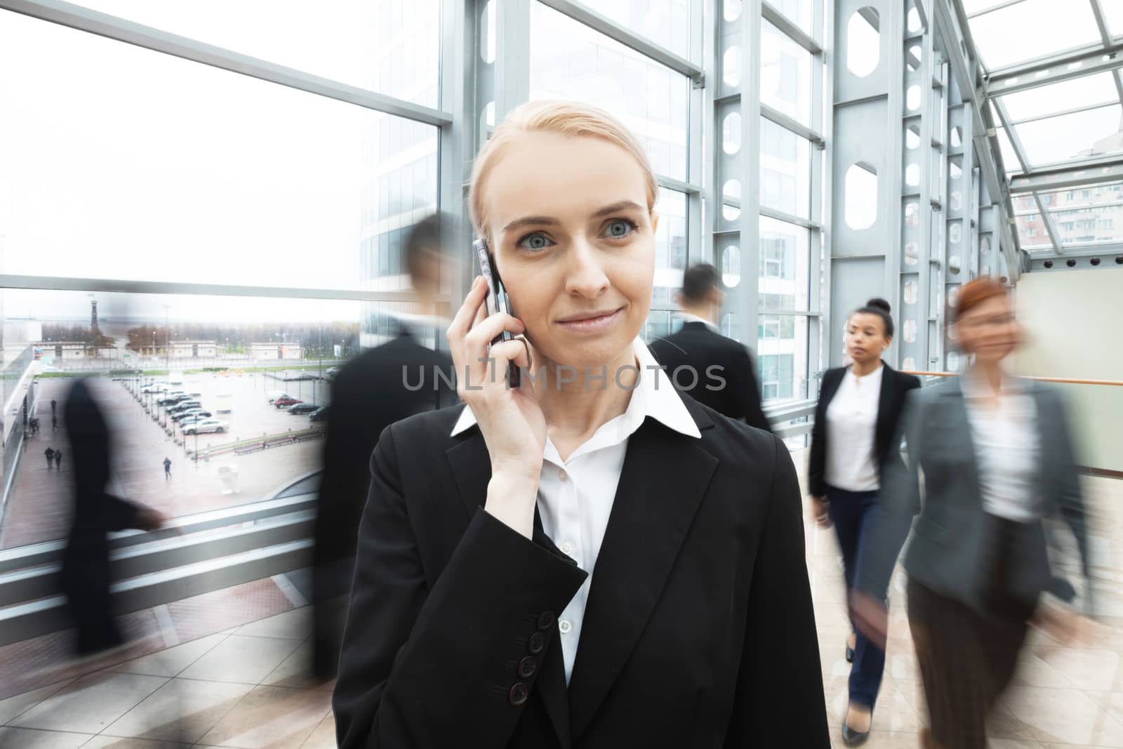 Business woman talking on phone standing in a crowd of walking people