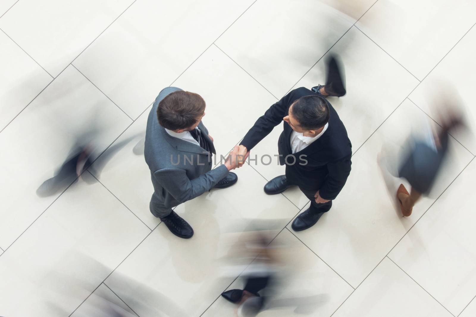 Business people shaking hands standing in a crowd of walking people, top view