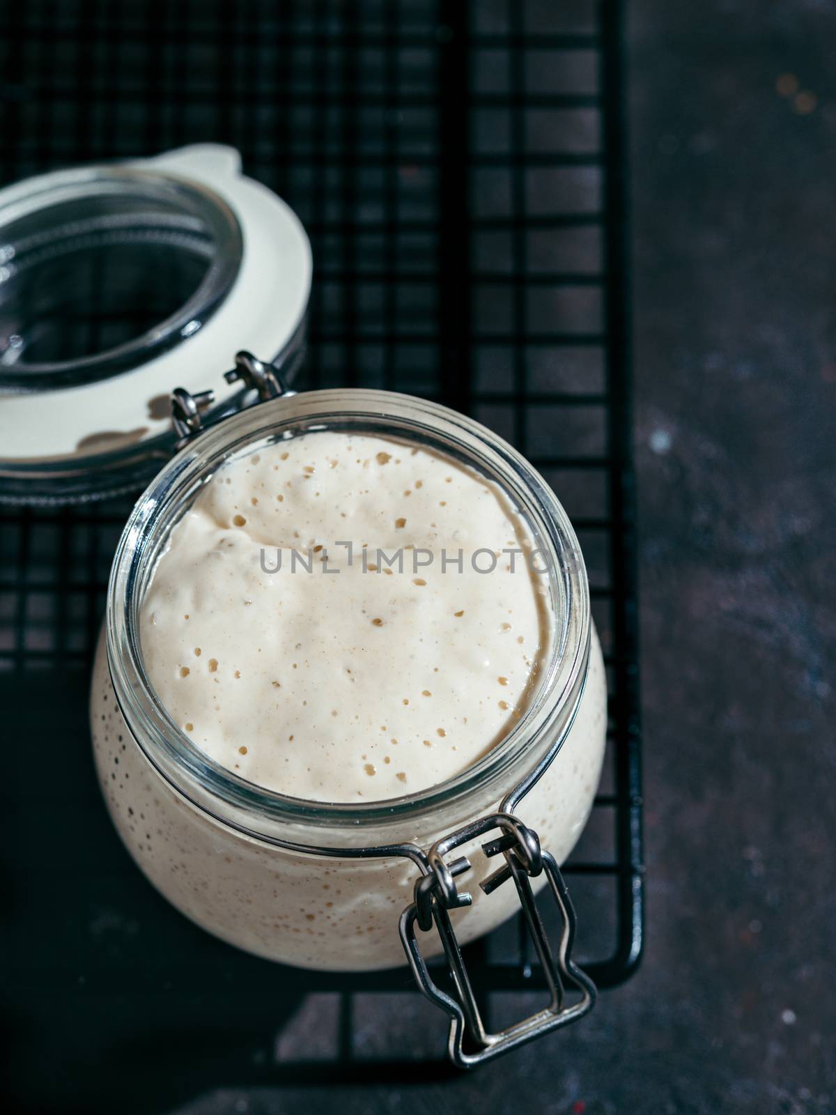 Wheat sourdough starter. Glass jar with sourdough starter on dark background, copy space. Vertical.