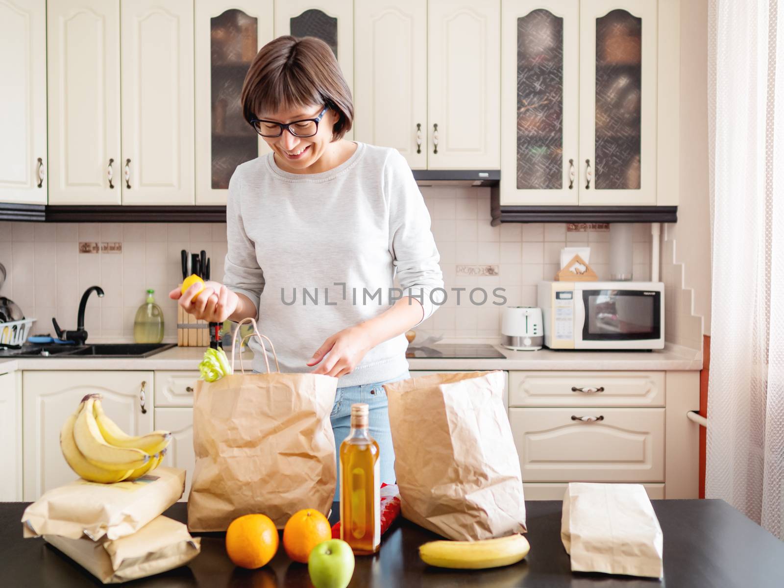 Woman sorts out purchases in the kitchen. Grocery delivery in paper bags. Subscription service from grocery store in conditions of quarantine because of coronavirus COVID19.