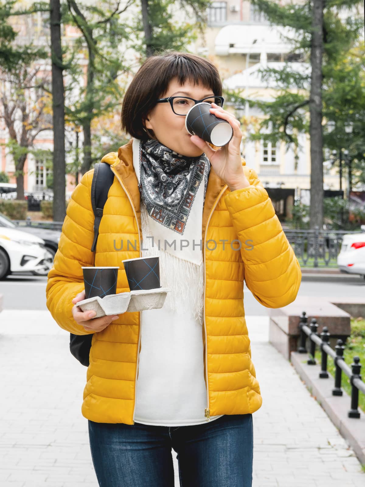 Take away coffee. Women in bright yellow jacket holds paper cup by aksenovko