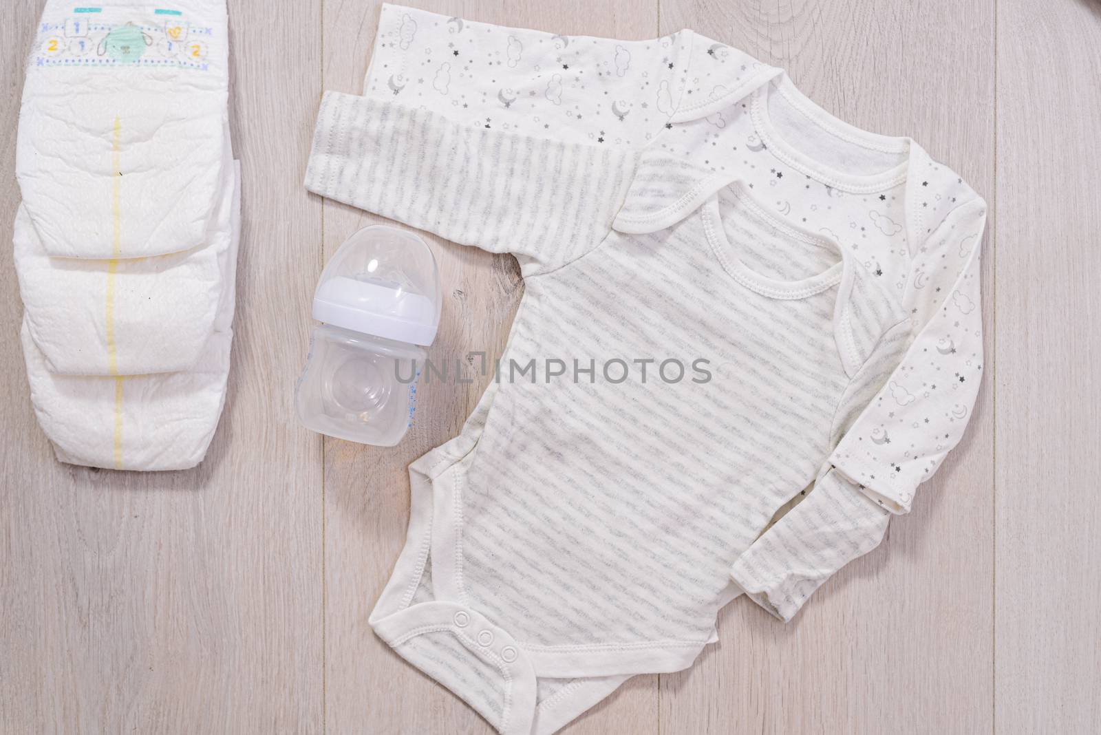 white baby clothes, diapers and baby milk bottle wooden background. newborn by jcdiazhidalgo